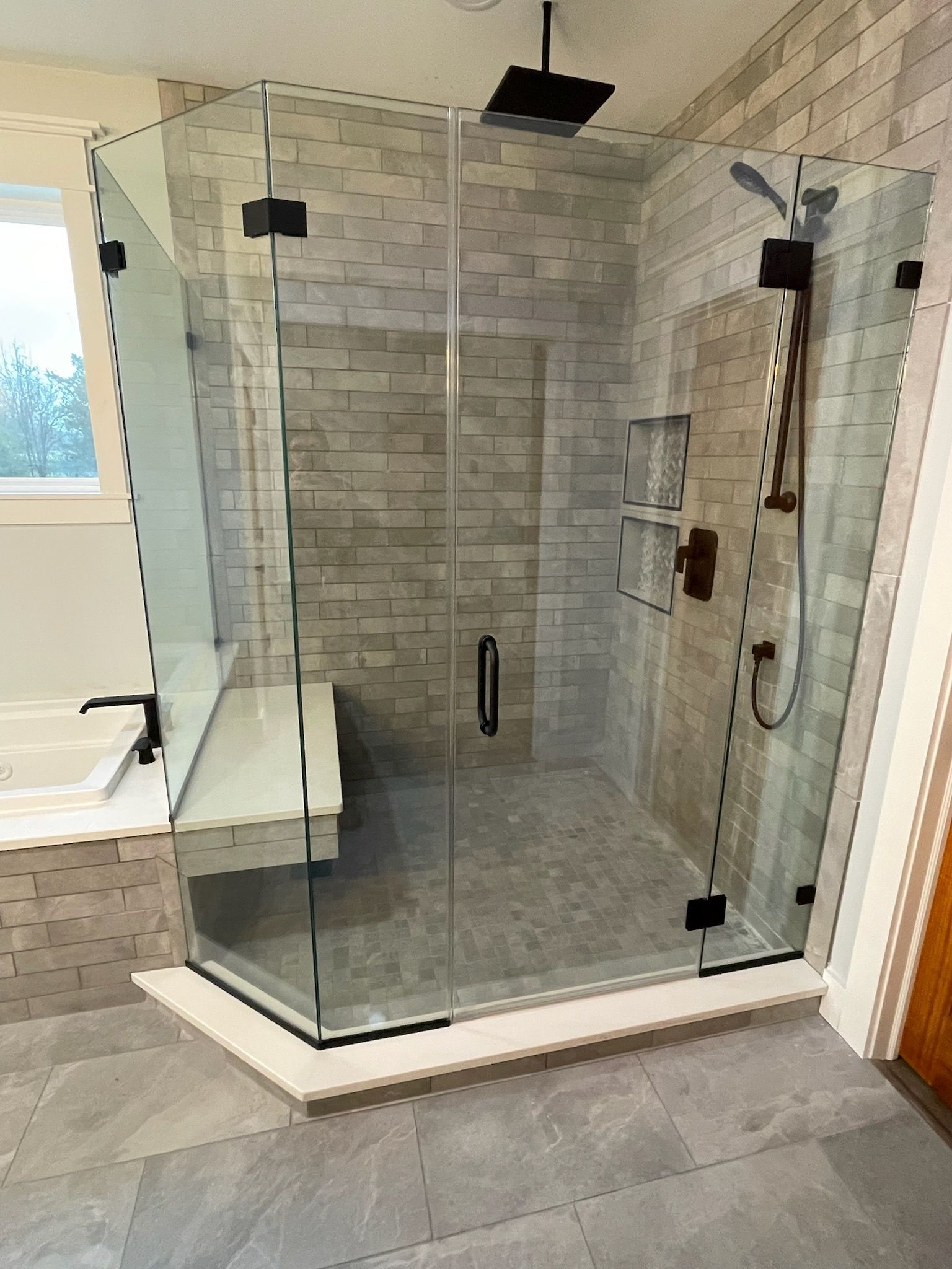 A modern, walk-in glass shower with black fixtures, stone tile walls, and an integrated bench in a bathroom.