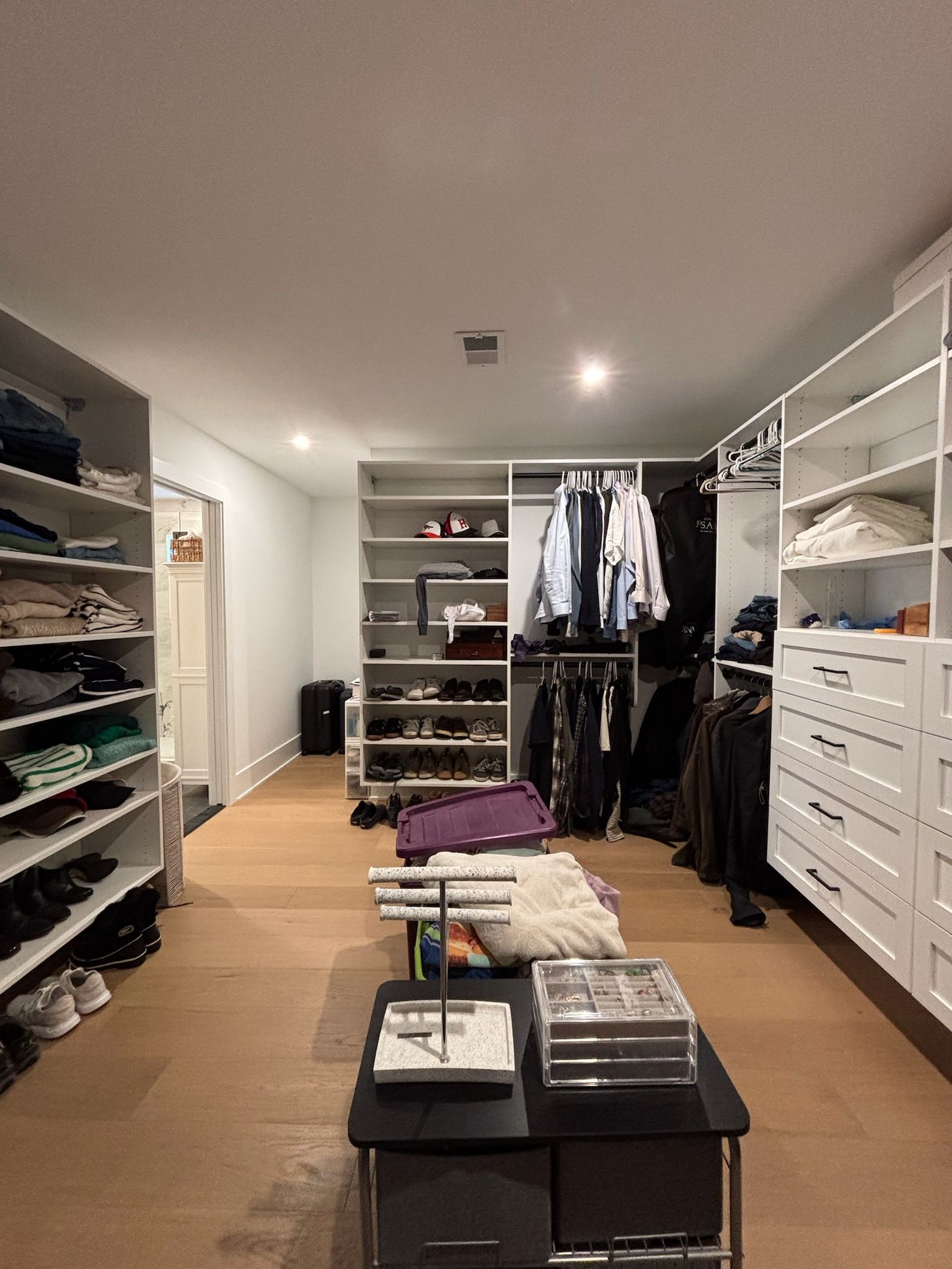 A spacious, modern walk-in closet with white shelving, hanging racks, a center island, and wood-look flooring.