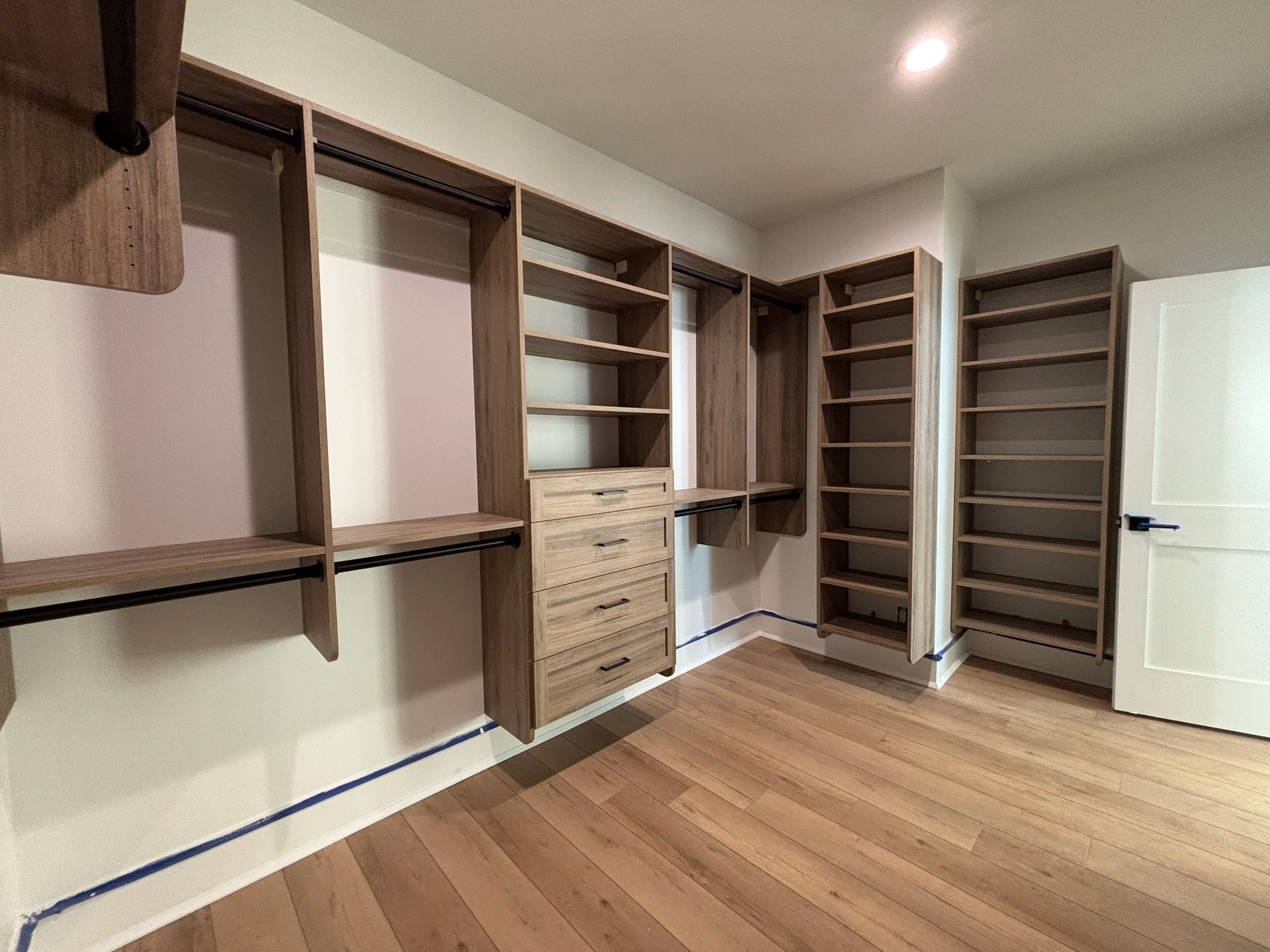A custom walk-in closet featuring light wood shelving, hanging rods, and a four-drawer unit against a light-colored wall.