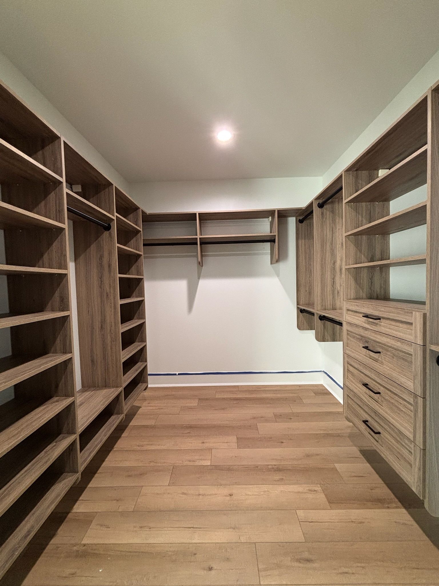 A walk-in closet featuring light-wood shelving units, hanging rods, and a built-in dresser against a white wall.