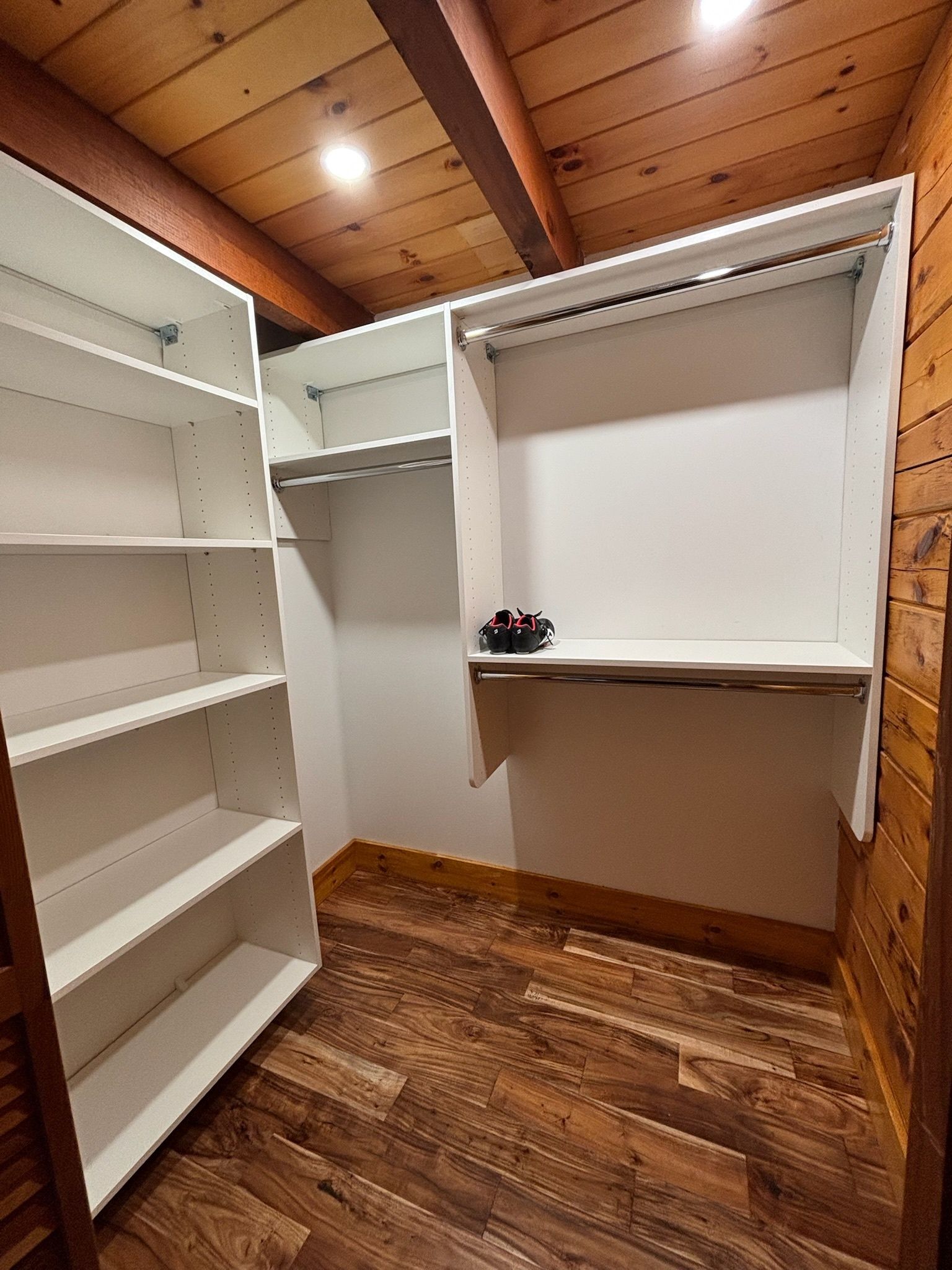 A walk-in closet featuring white modular shelving, hanging rods, and a dark wood-paneled wall and floor.