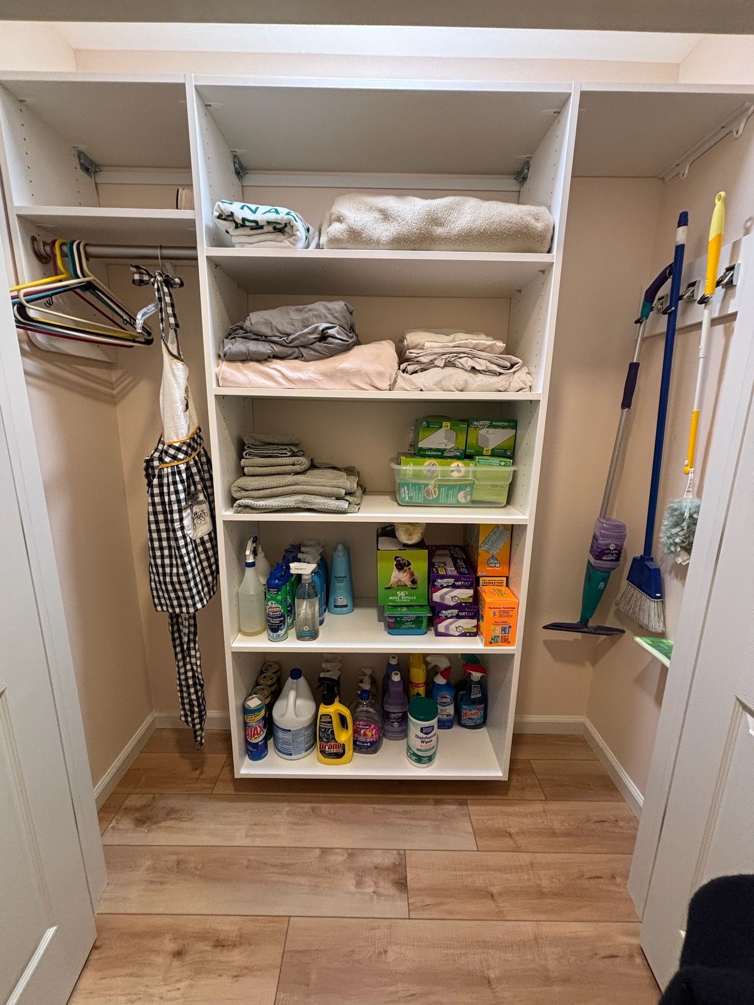 A white shelving unit inside a closet, filled with organized cleaning supplies, towels, and linens.