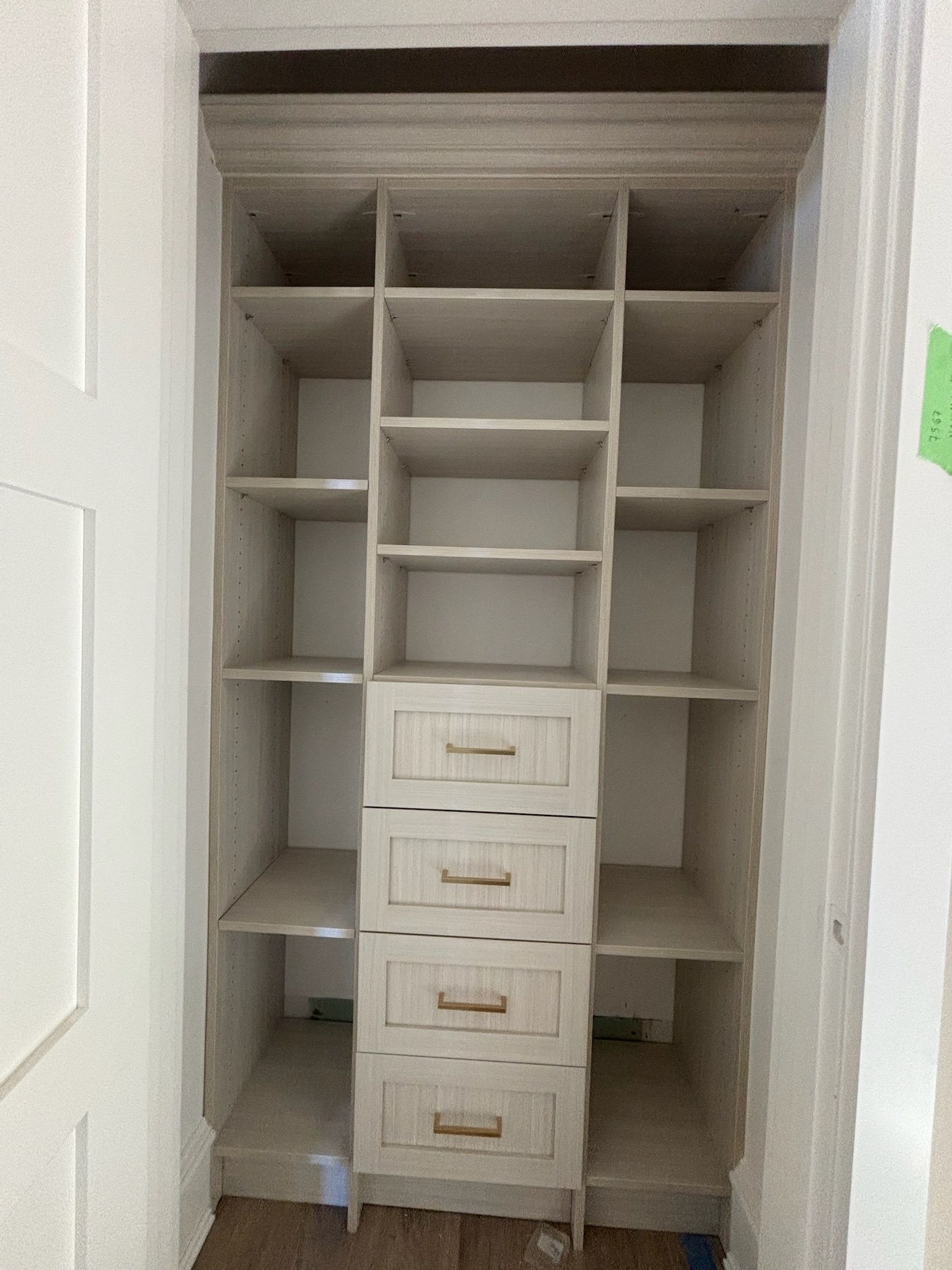 A custom-built, light-colored wooden closet organizer featuring open shelving and a central column of four drawers.