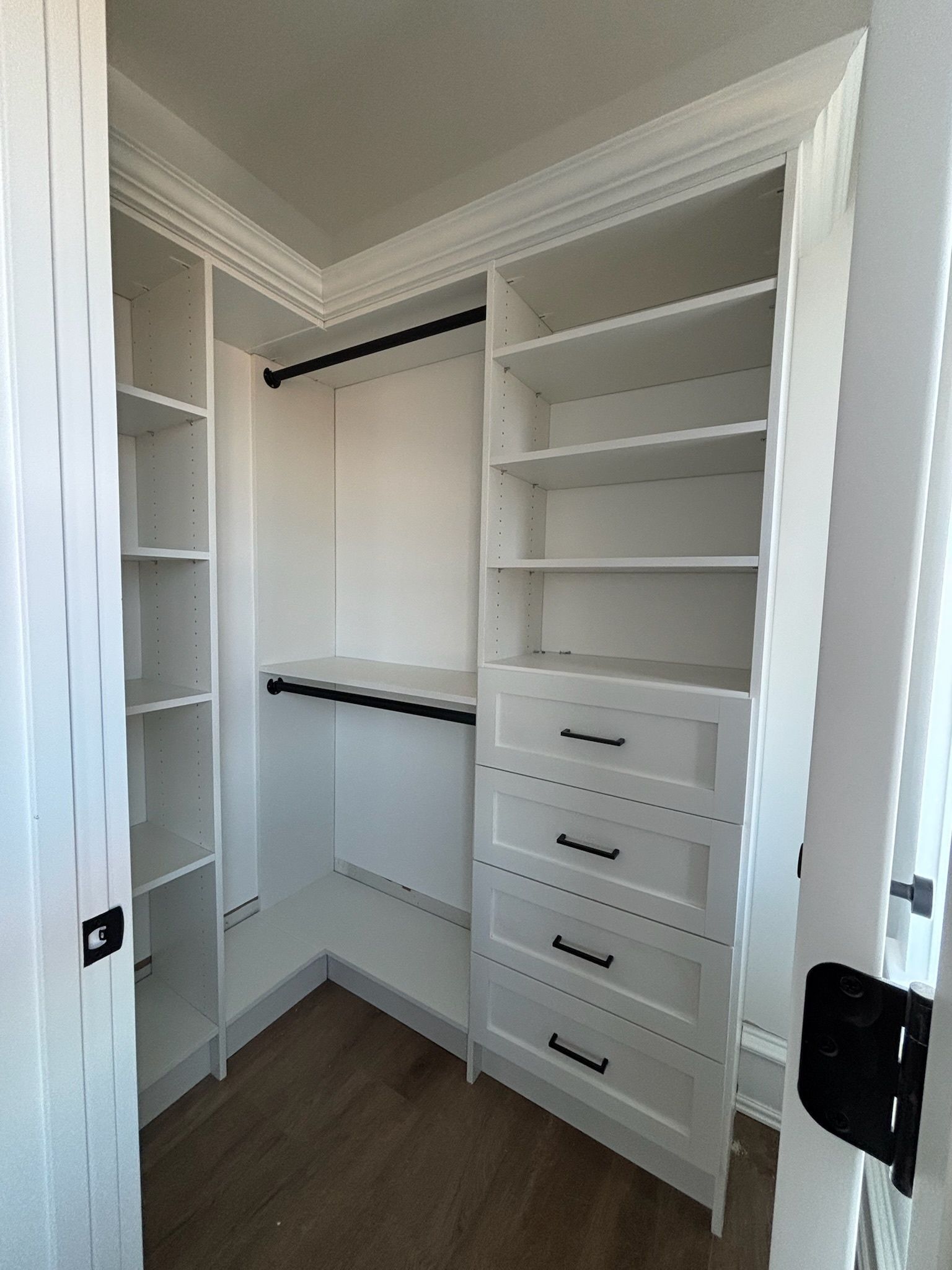 A small walk-in closet featuring white shelving, a hanging rod, and a four-drawer dresser with black hardware.