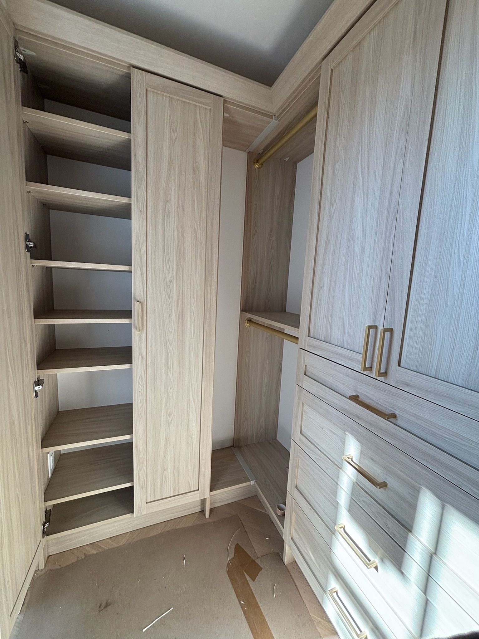 A walk-in closet featuring light-wood cabinetry, shelves on the left, a hanging rod in the back, and drawers on the right.