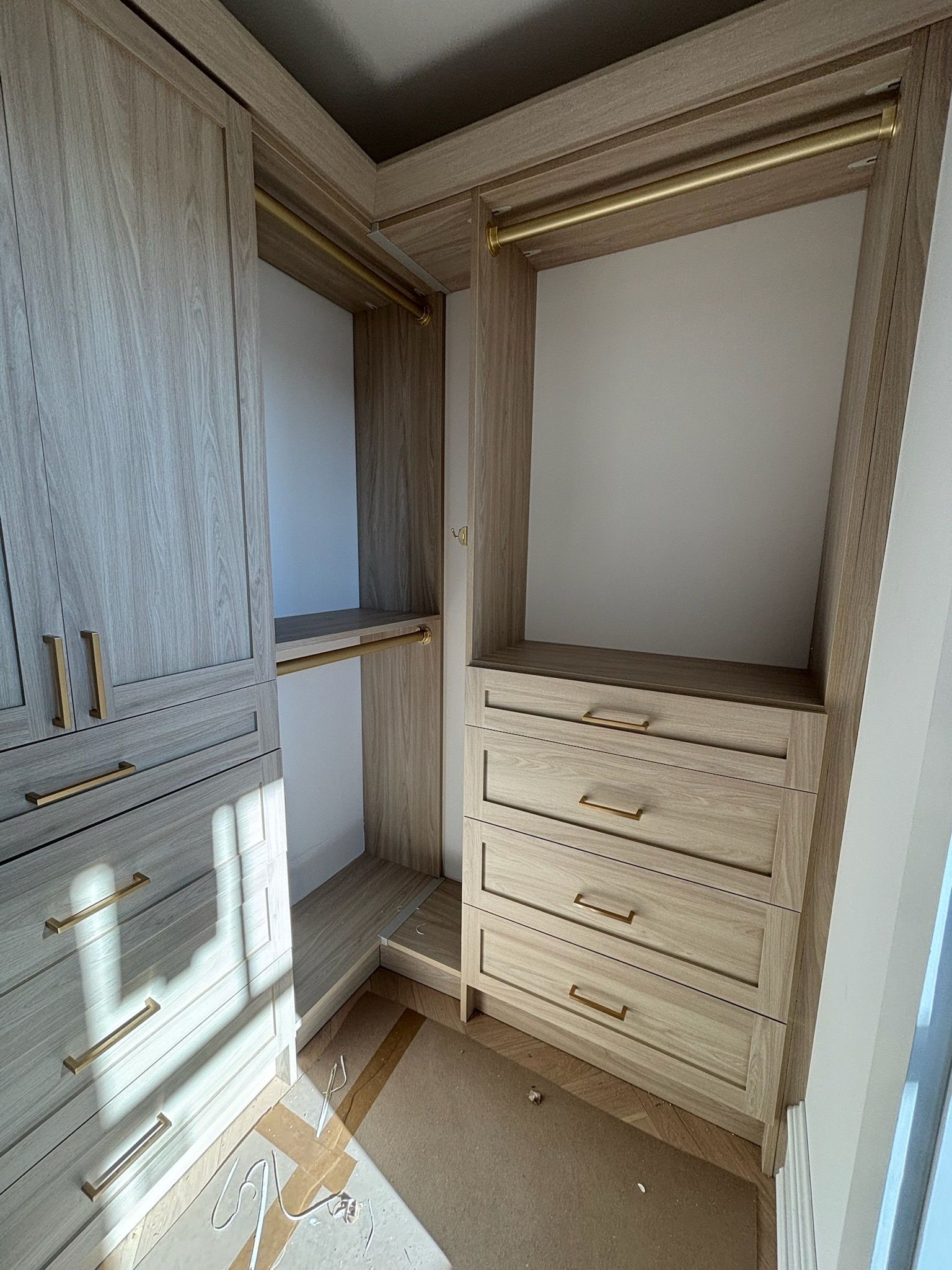 A light-wood, L-shaped closet interior featuring a hanging rod, open shelving, and a set of three deep drawers.