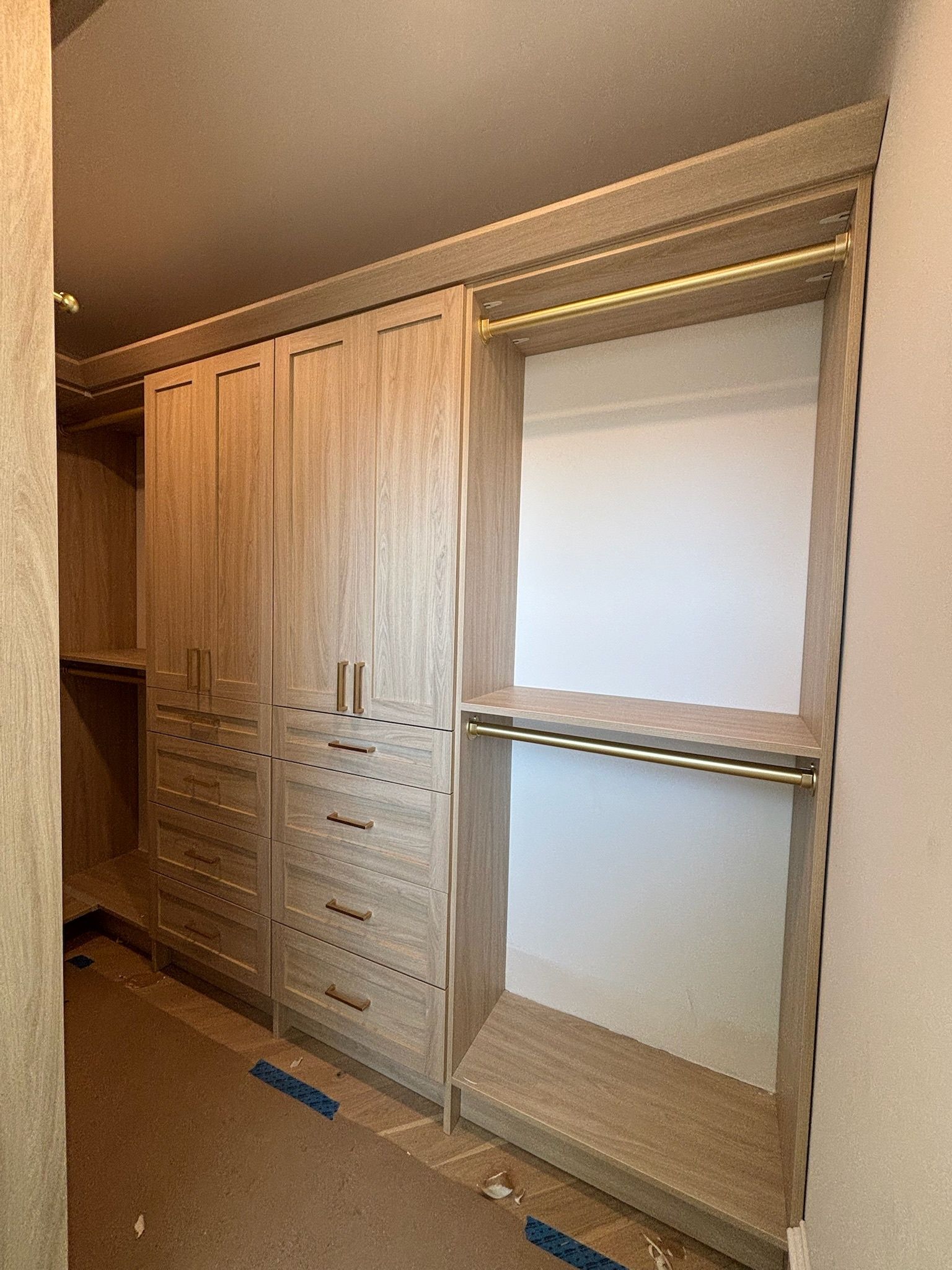A walk-in closet featuring light oak-finish cabinetry, including two doors with stacked drawers and open hanging rods.