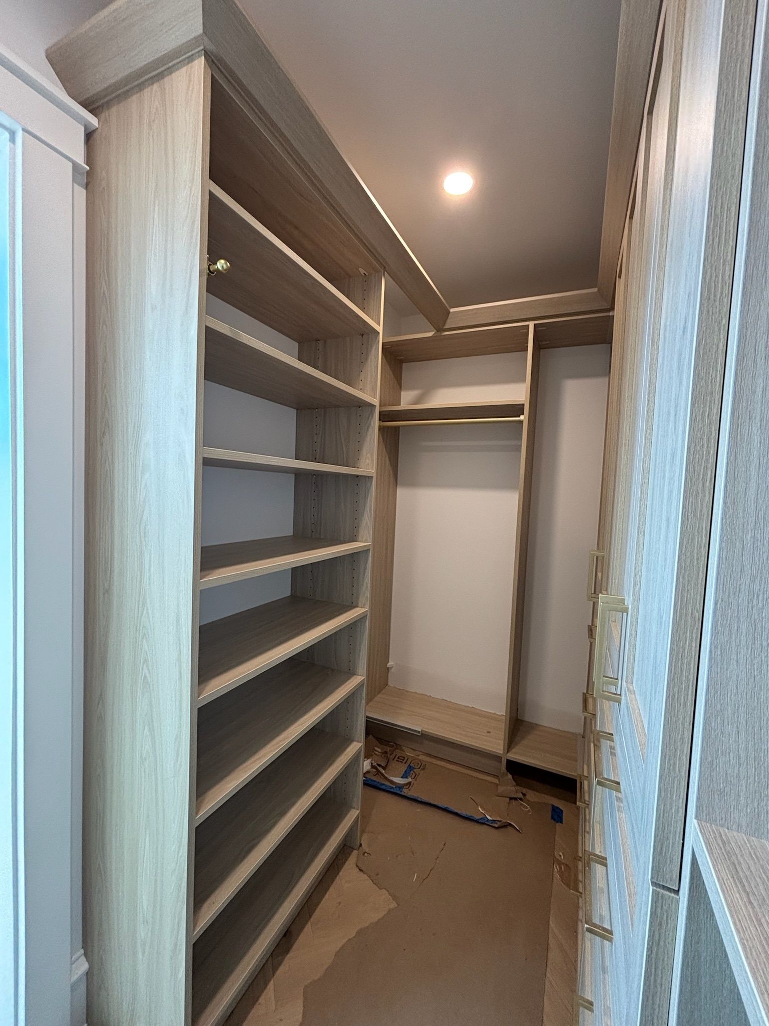 A light wood-toned walk-in closet under construction, featuring multiple shelving units and a hanging rod.