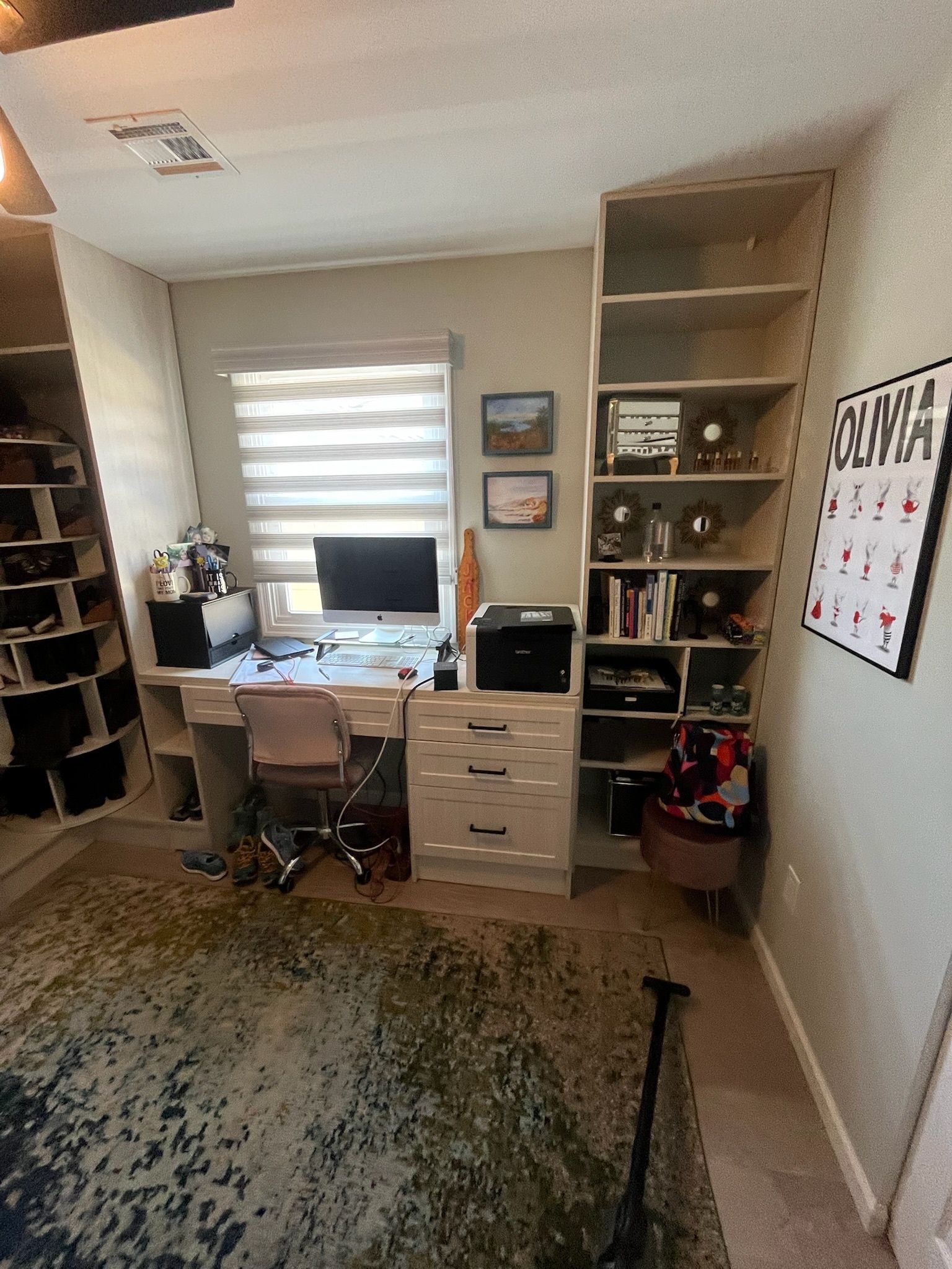A home office with a computer desk, printer, built-in shelving unit, and a patterned area rug in a room with a window.