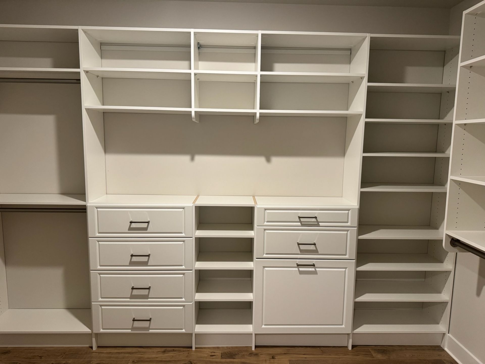 A modern white walk-in closet system featuring hanging space, open shelving, and a combination of drawers and cabinets.