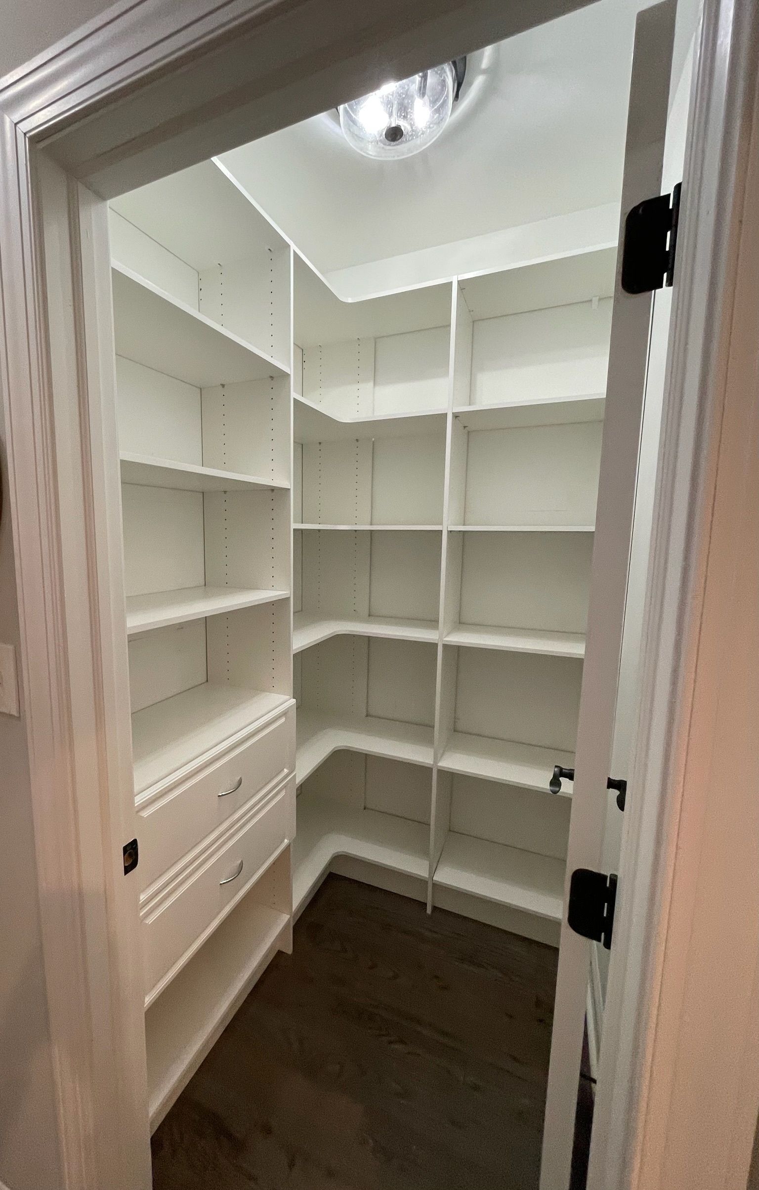 A small, empty walk-in pantry with white shelves, two drawers, and a ceiling light.