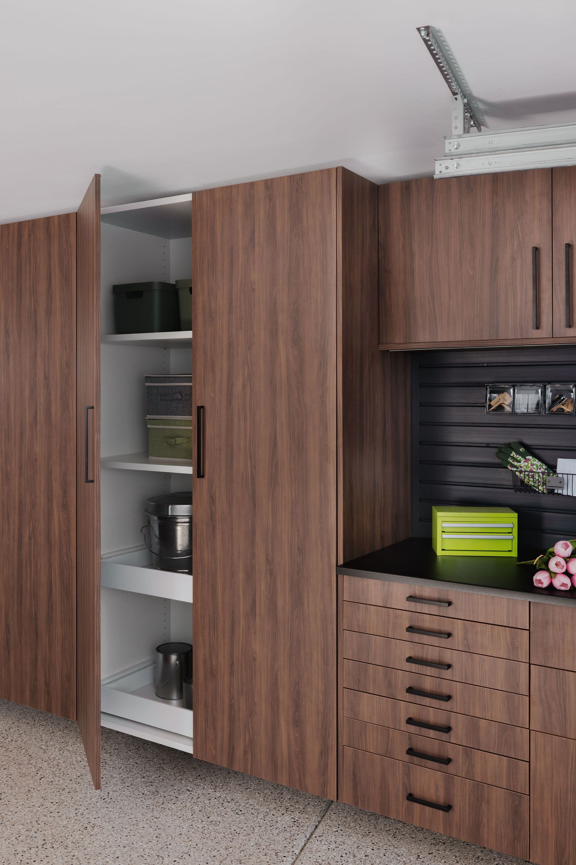 Dark wood storage cabinets with open shelves and drawers in a garage setting with a slat wall work area.