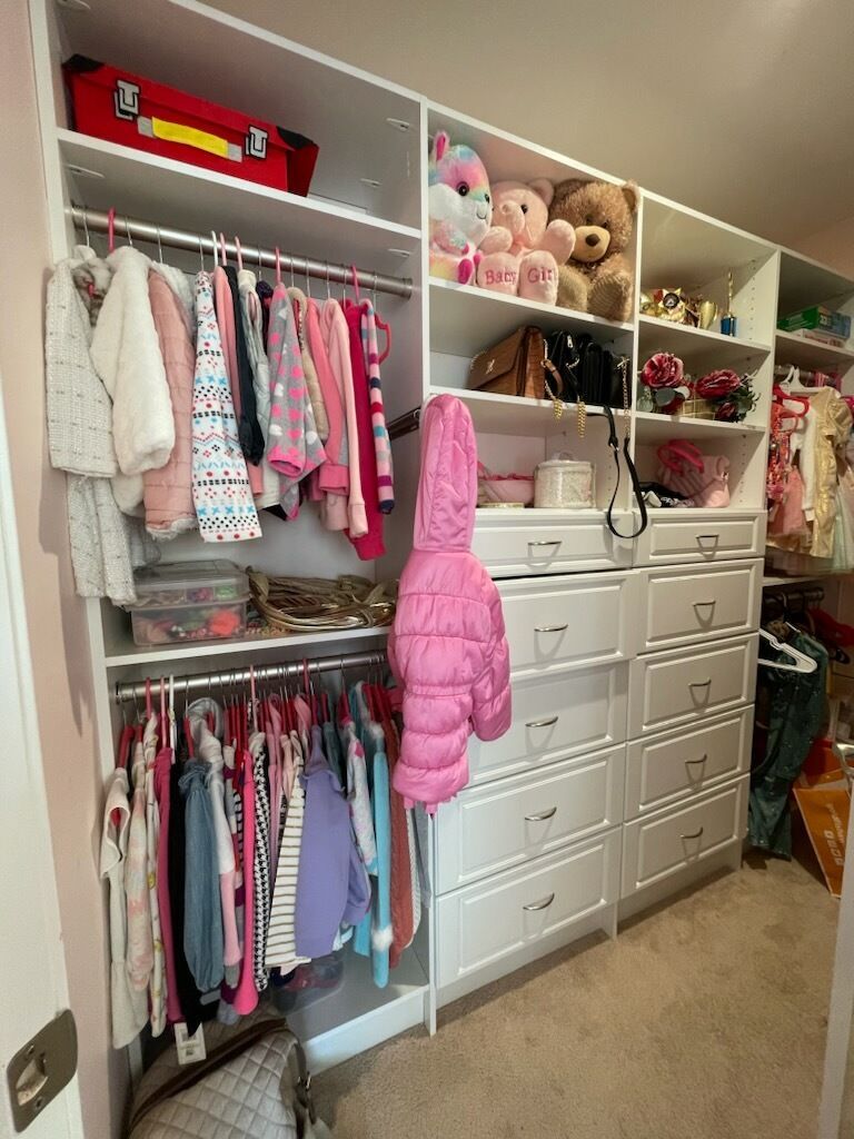 A white, organized bedroom closet featuring hanging clothes on two levels, open shelving for toys, and built-in drawers.