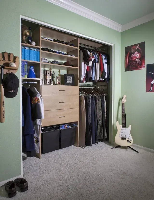 A closet with custom shelving and drawers. Clothes hang on rods. A guitar leans against a wall in a room with green walls.