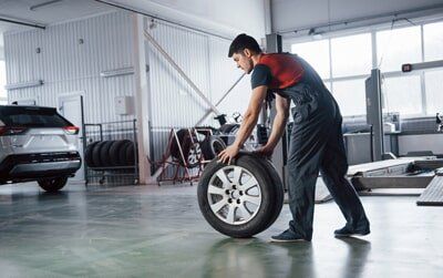 Worker Rolling Tyre Across Garage — Tyre Service in Springsure, QLD