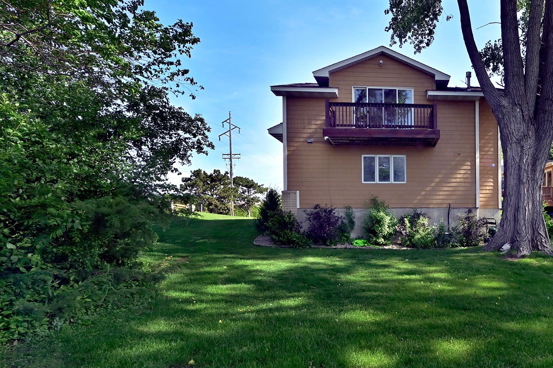 A house with a balcony sits in the middle of a lush green field