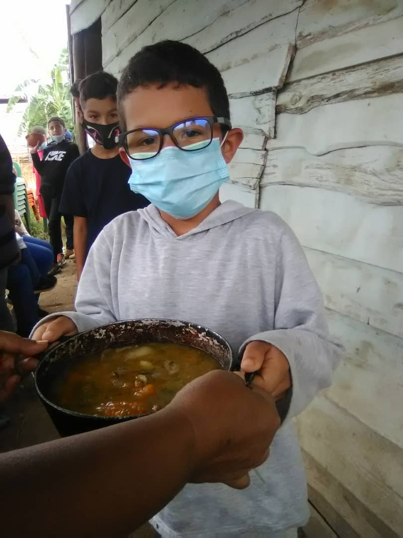 Young Venezuelan boy wearing a mask getting a bowl of soup in an impoverished community