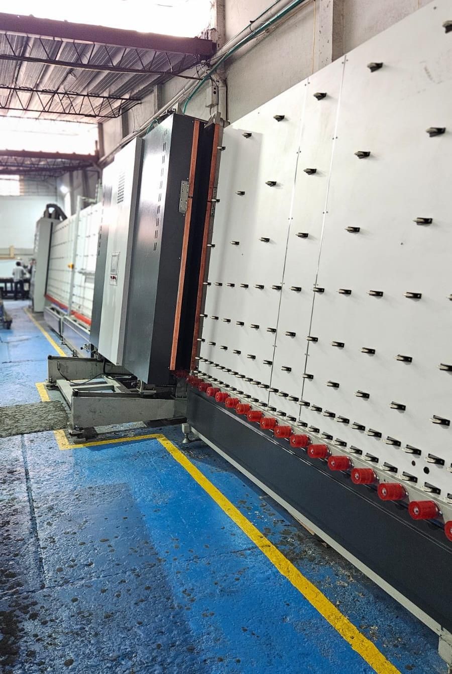 Gran máquina industrial de procesamiento de vidrio en un entorno de fábrica, con múltiples paneles visibles.