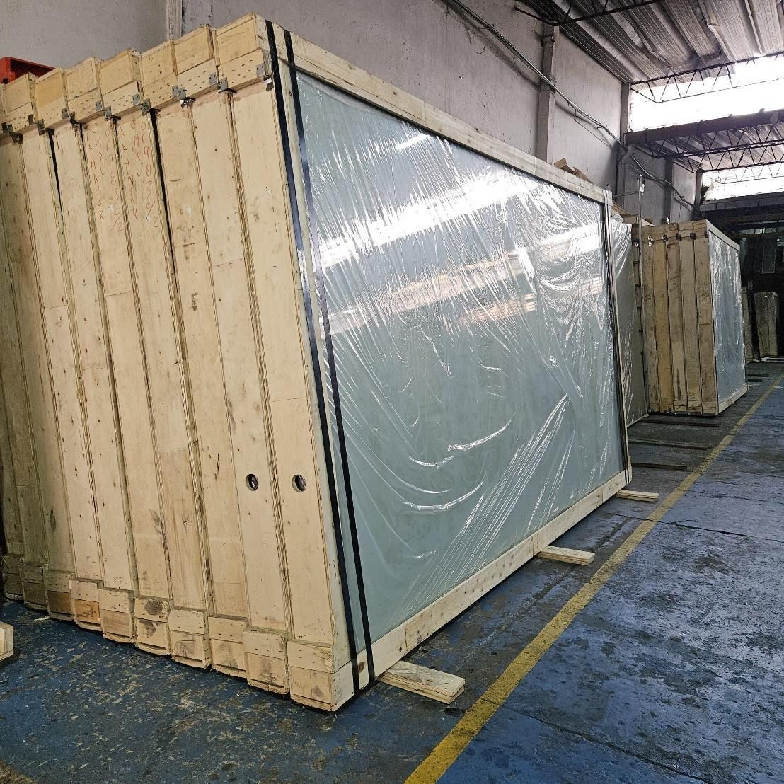 Cajas de madera que contienen grandes paneles de vidrio, envueltos en plástico, en un almacén.