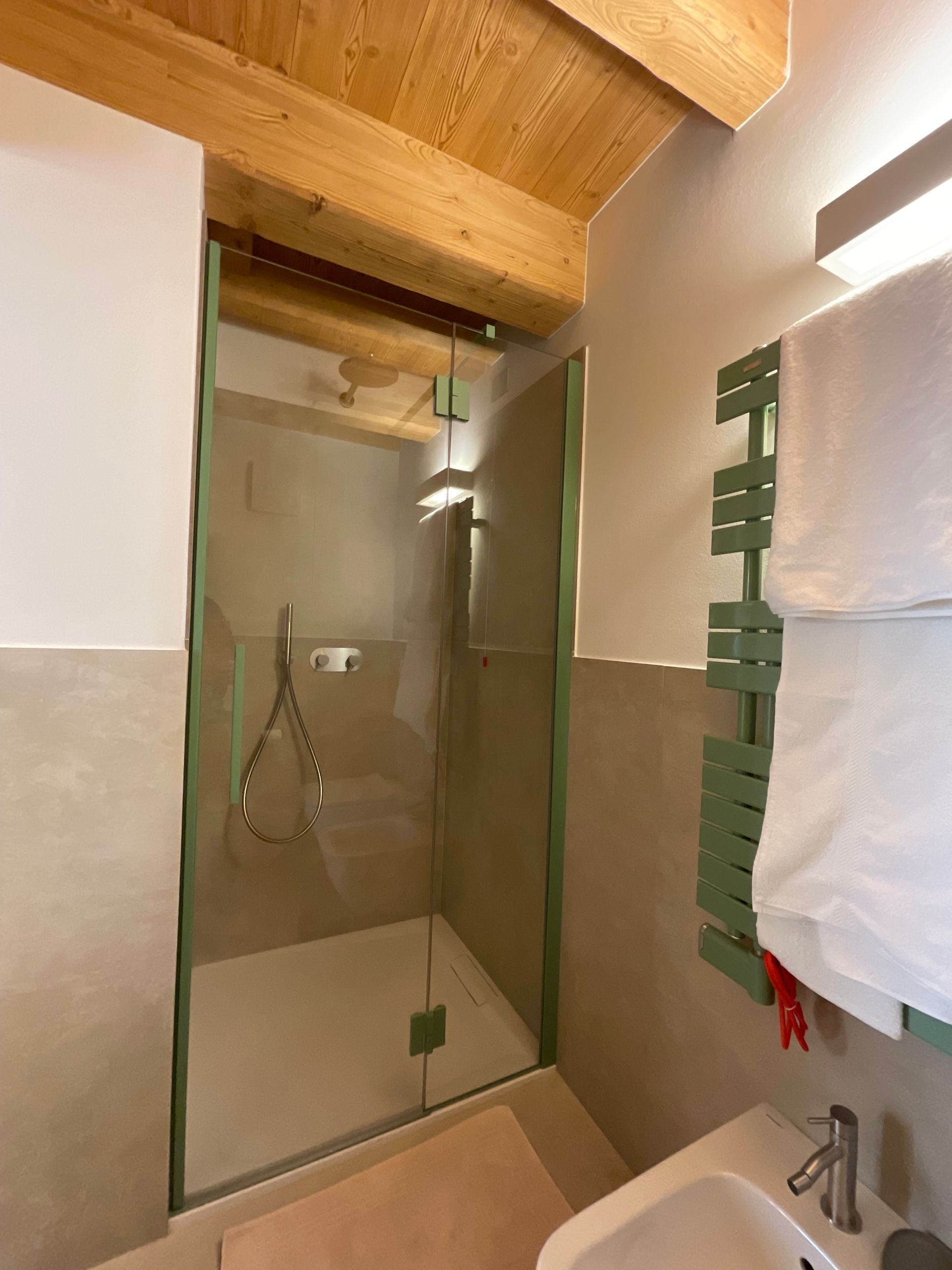 Doccia con finiture verdi, portasciugamani e travi in ​​legno al soffitto.