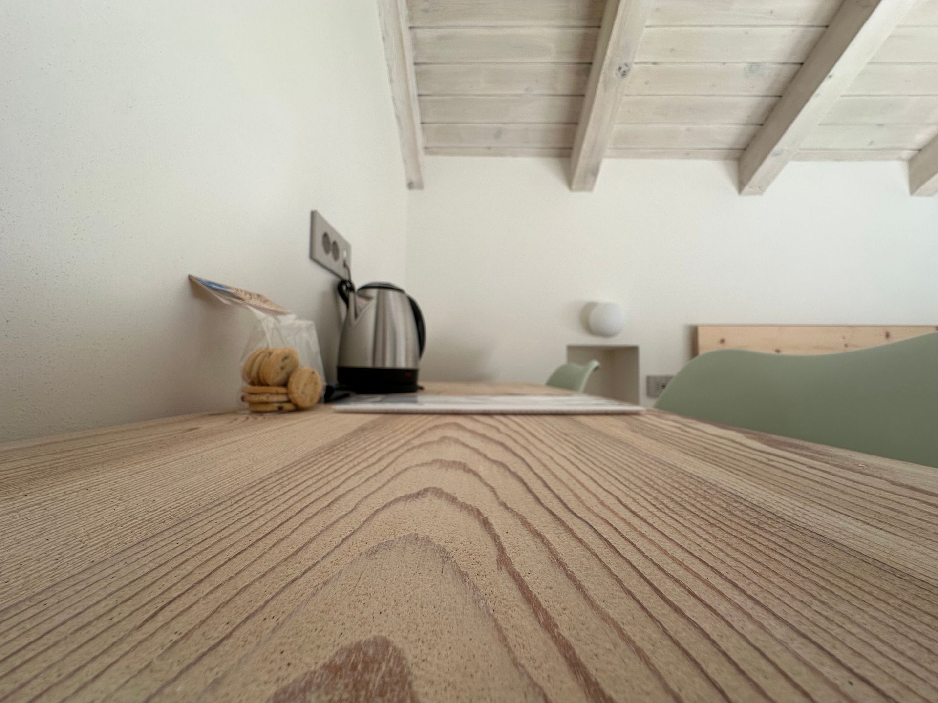 In primo piano un tavolo in legno; sullo sfondo un bollitore, degli snack e una presa elettrica sulla parete.