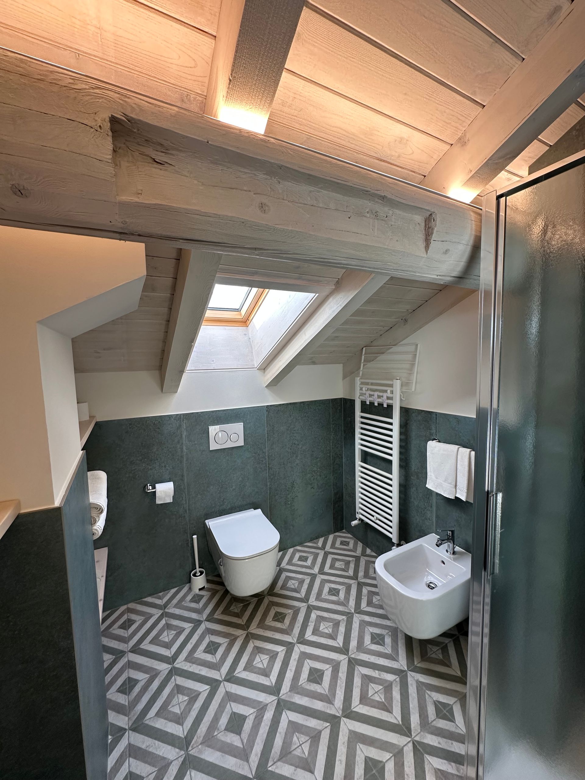 Bagno con soffitto spiovente, WC, bidet e pavimento in piastrelle fantasia.