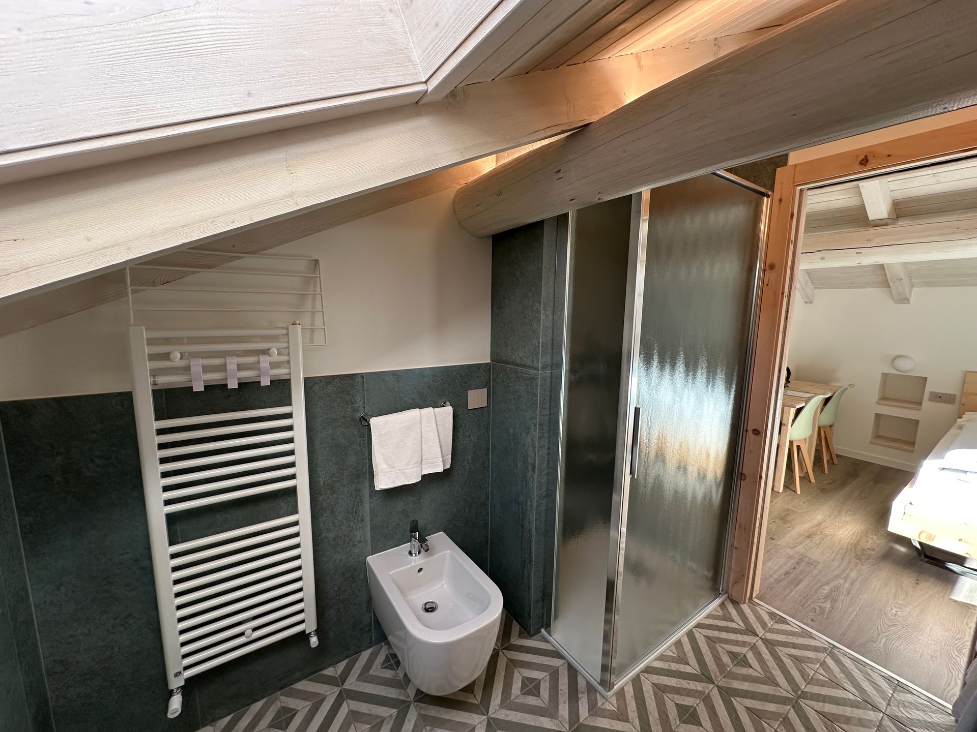 Bagno con bidet, doccia e scaldasalviette. Il pavimento è decorato con motivi geometrici e la camera da letto è a vista.