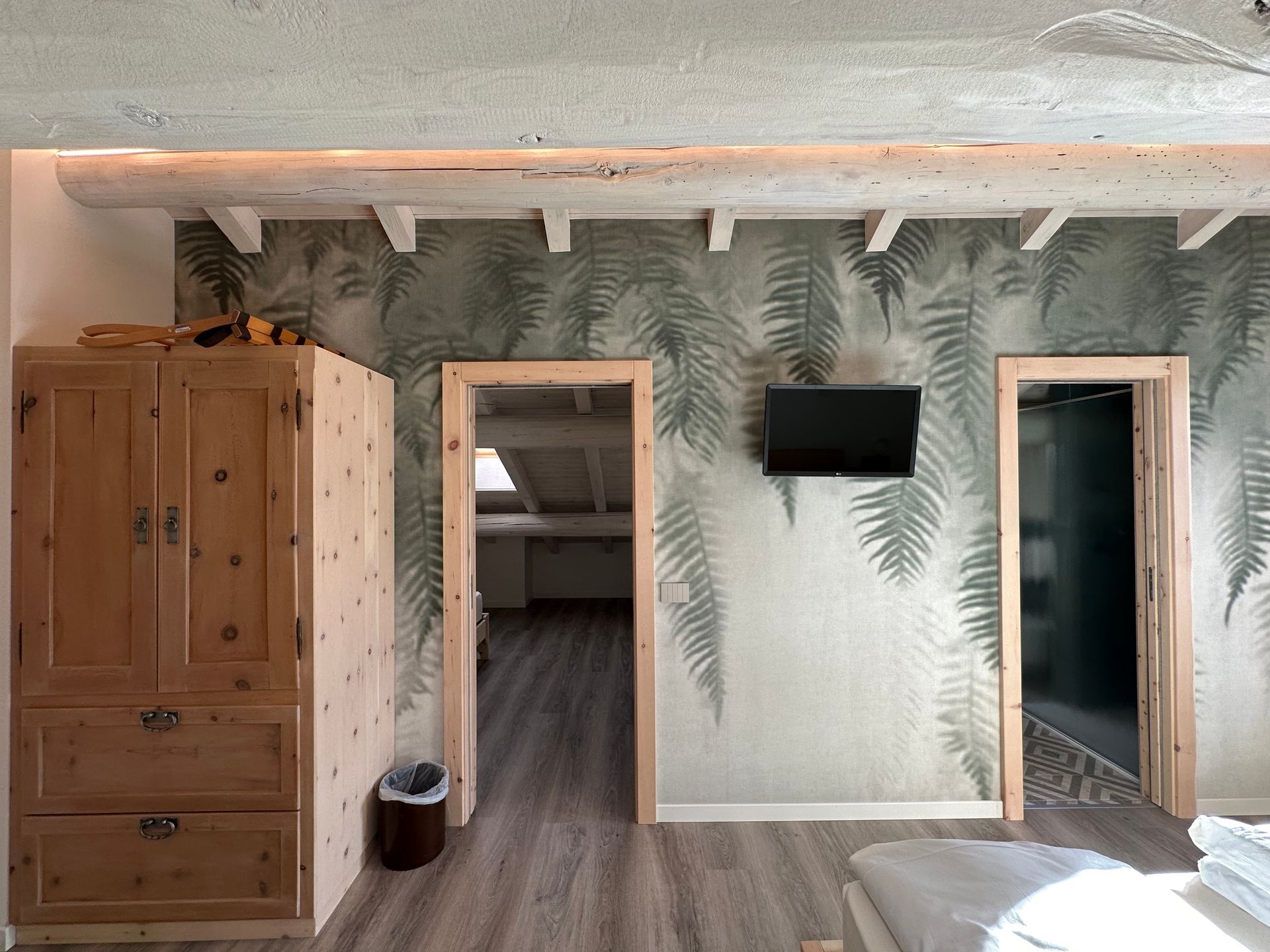 Camera da letto con armadio in legno, carta da parati con motivi di felci e due porte.