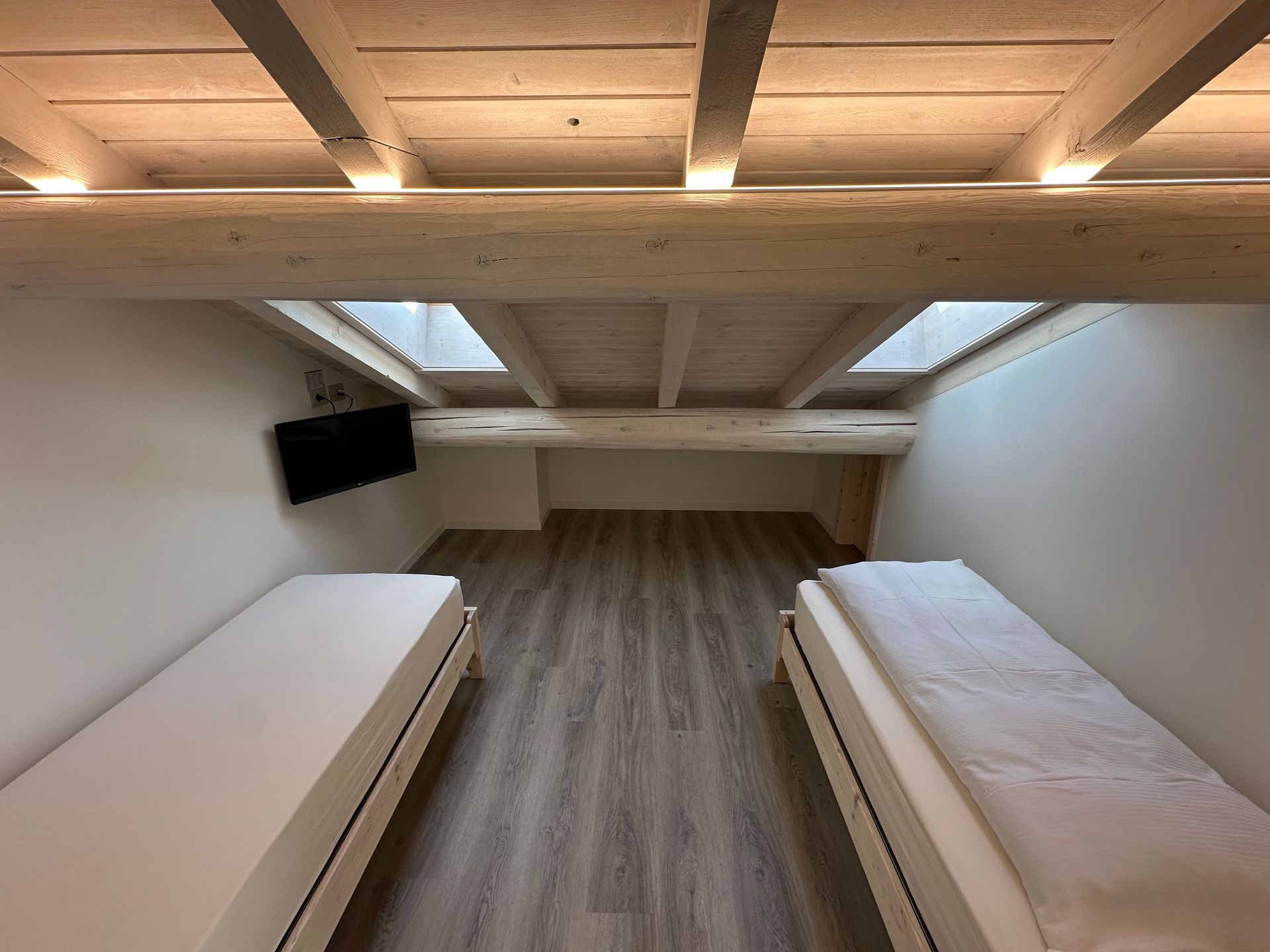 Camera da letto con due letti singoli, TV e soffitto con travi in ​​legno.