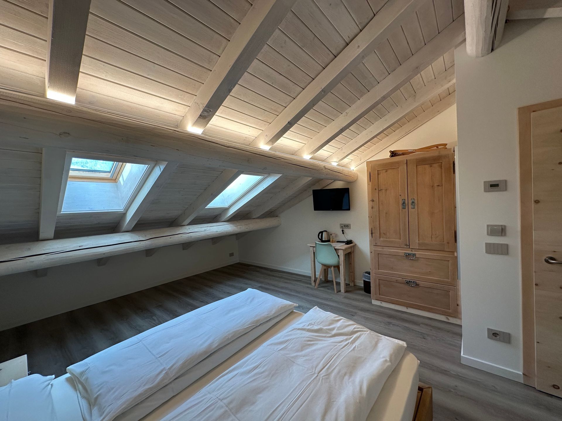 Camera da letto con soffitto spiovente, lucernari, letto, scrivania e armadio in legno.