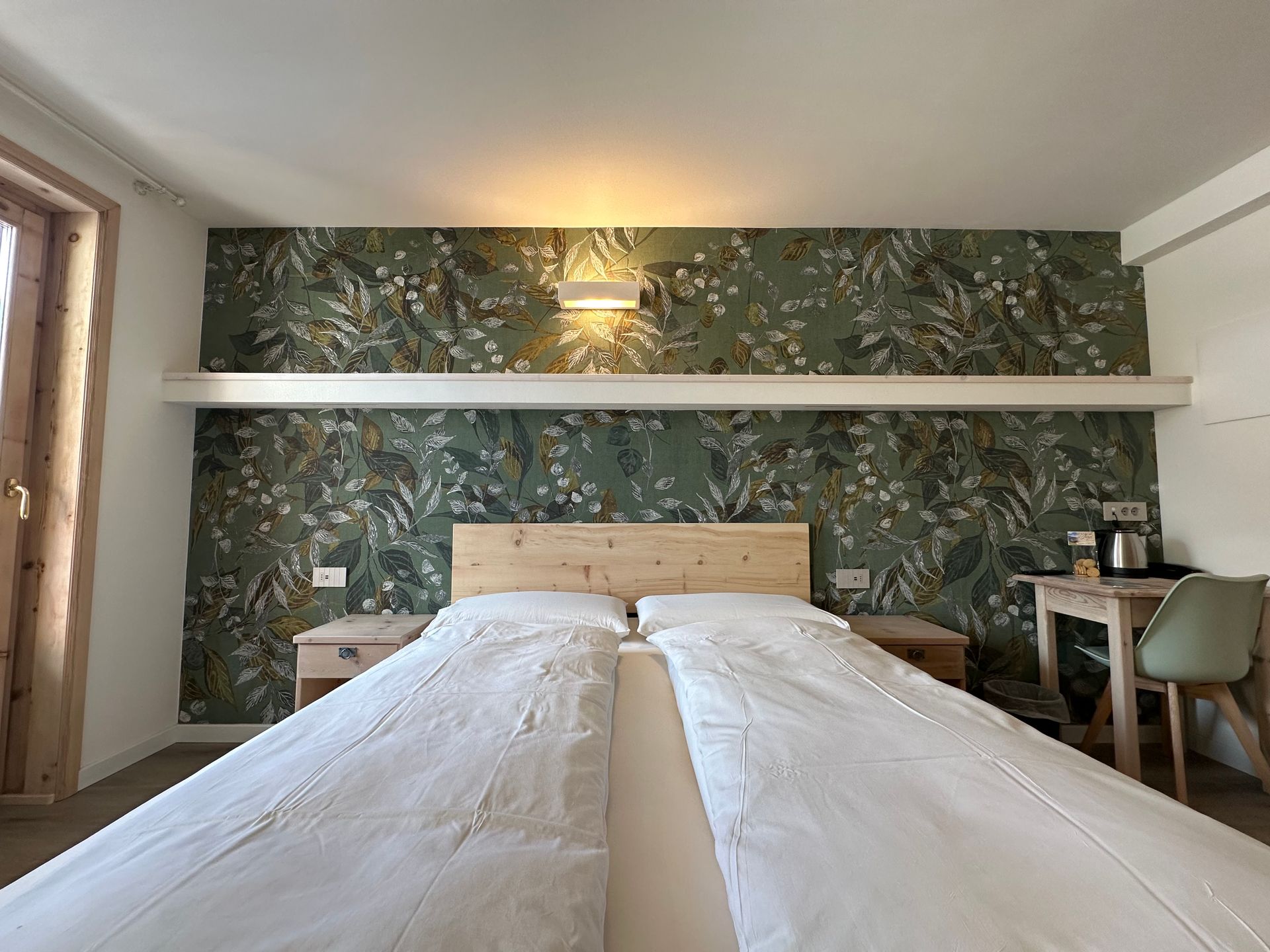 Camera da letto con due letti singoli, parete decorativa con carta da parati floreale, comodini, scrivania e lampada.