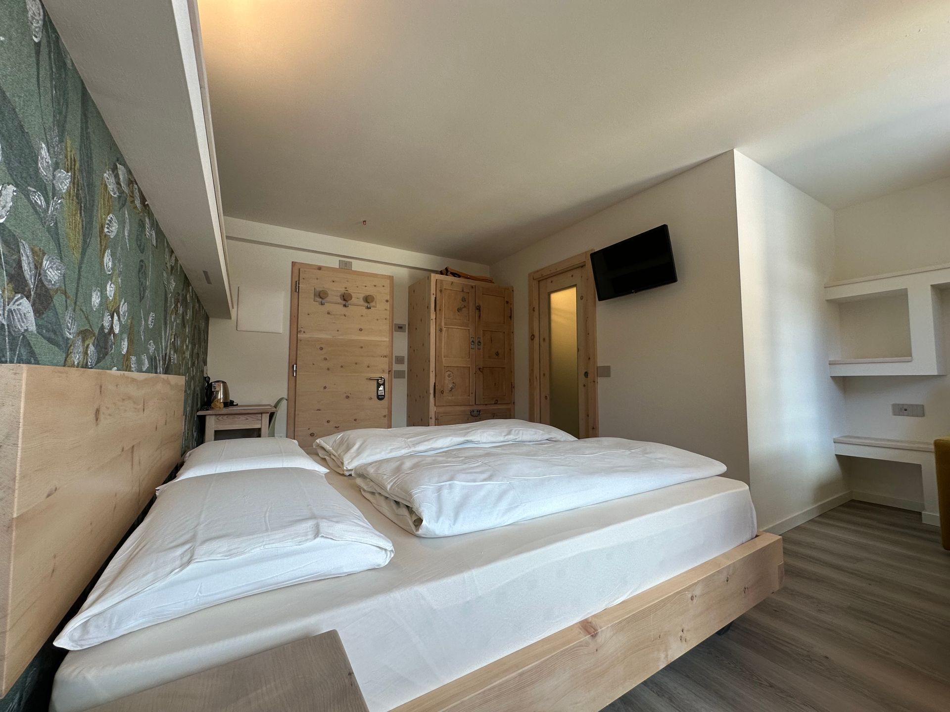 Camera da letto con letto, armadi e pareti in legno chiaro. È installata una piccola TV.