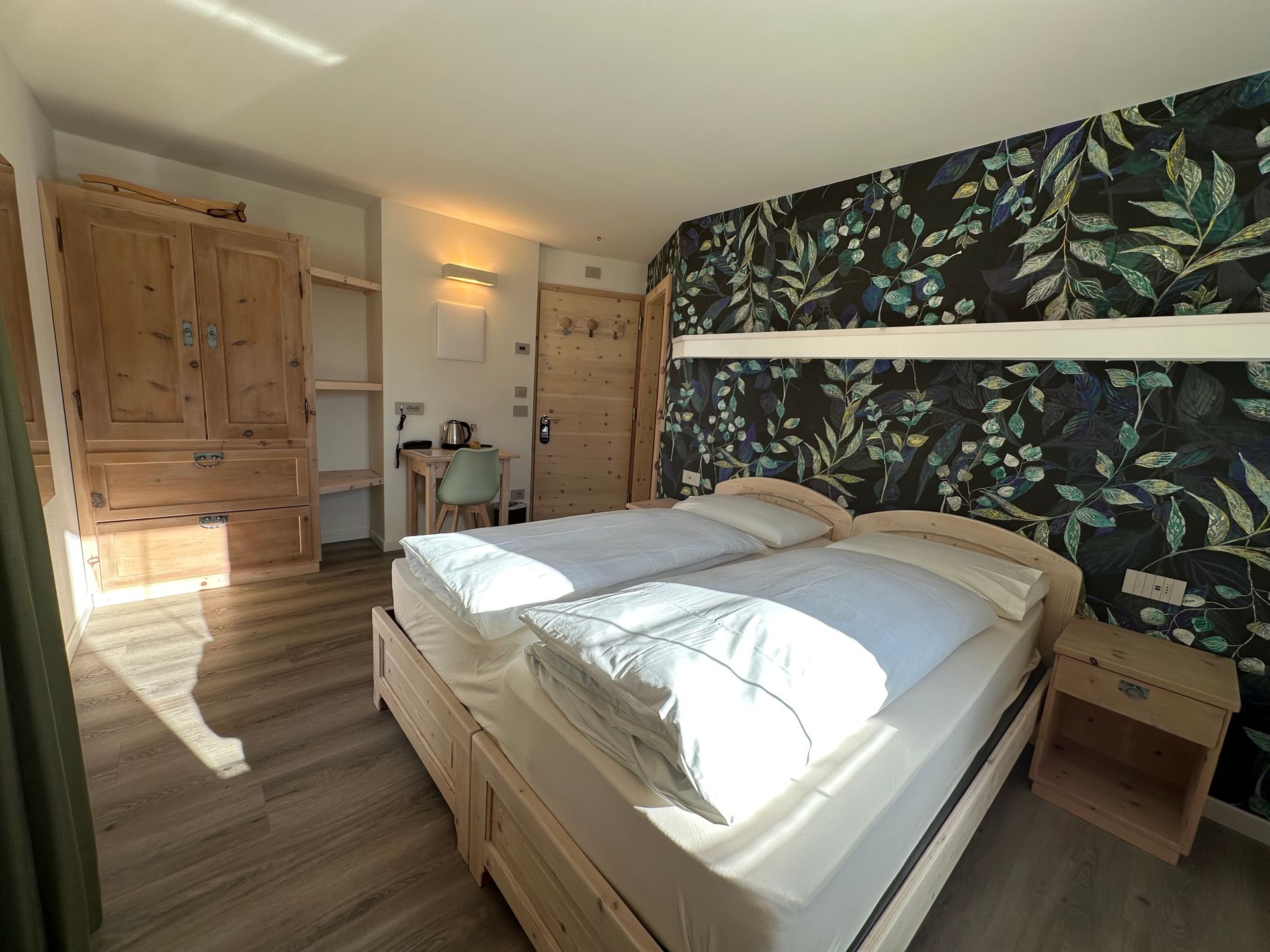 Camera da letto con due letti, mobili in legno e carta da parati floreale.