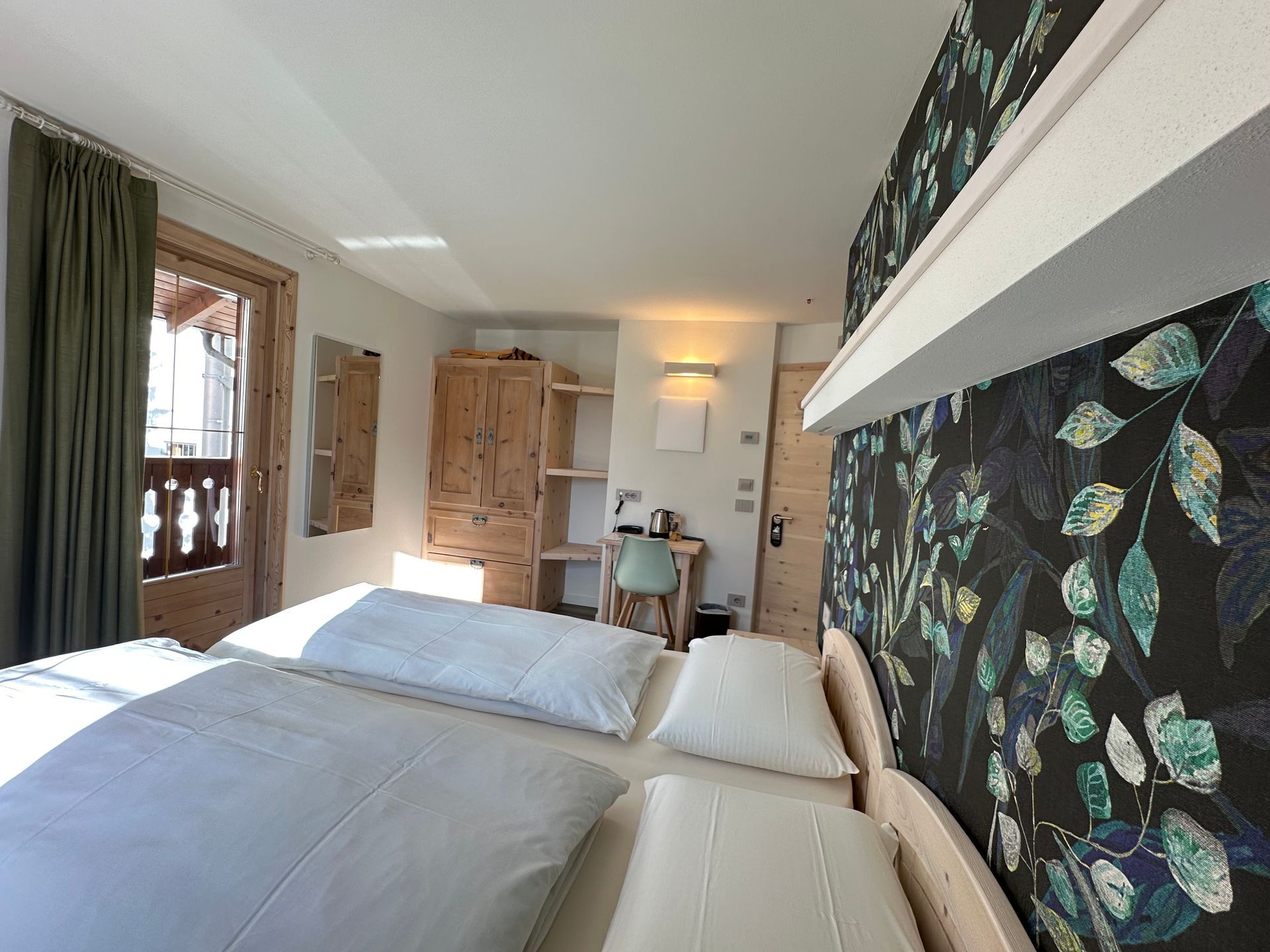 Camera da letto con due letti, mobili in legno, carta da parati floreale e balcone.