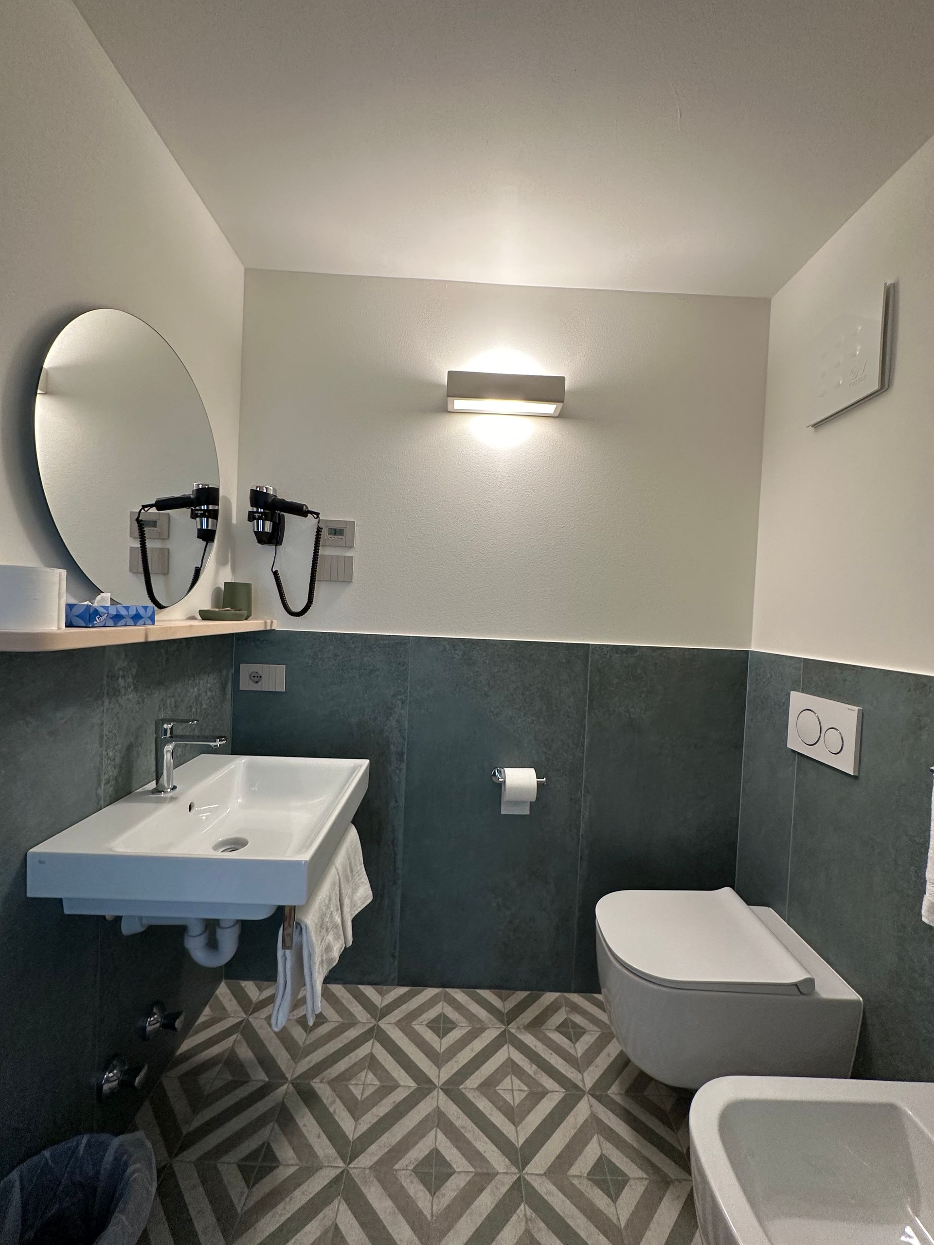 Bagno moderno con lavandino e WC bianchi e pareti piastrellate color verde acqua. Pavimento con motivi decorativi.