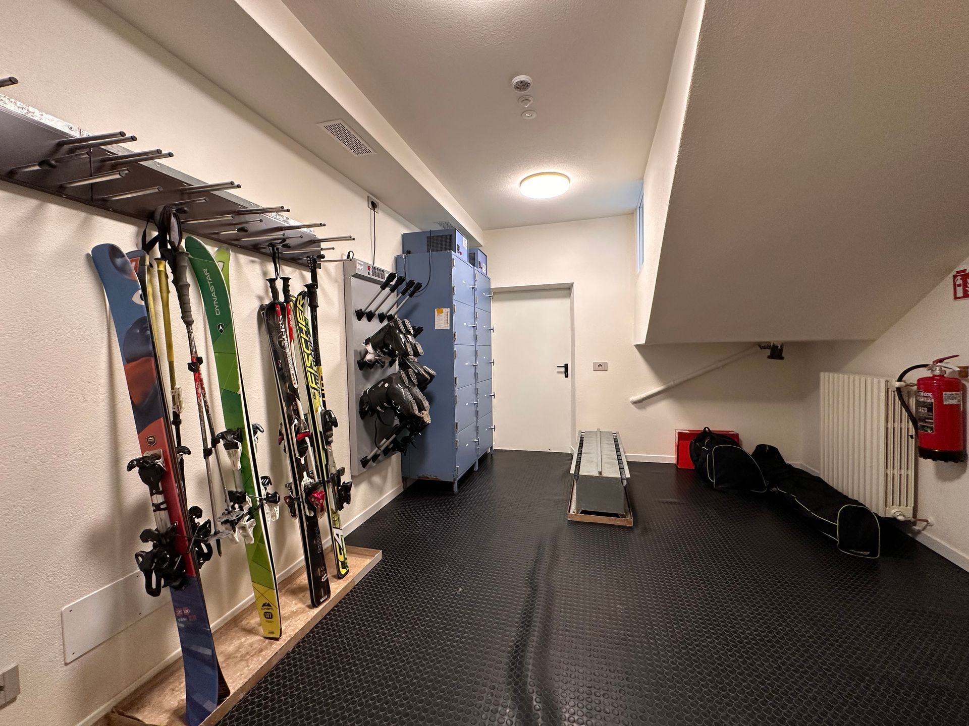Deposito sci con rastrelliere, armadietti blu e scale.