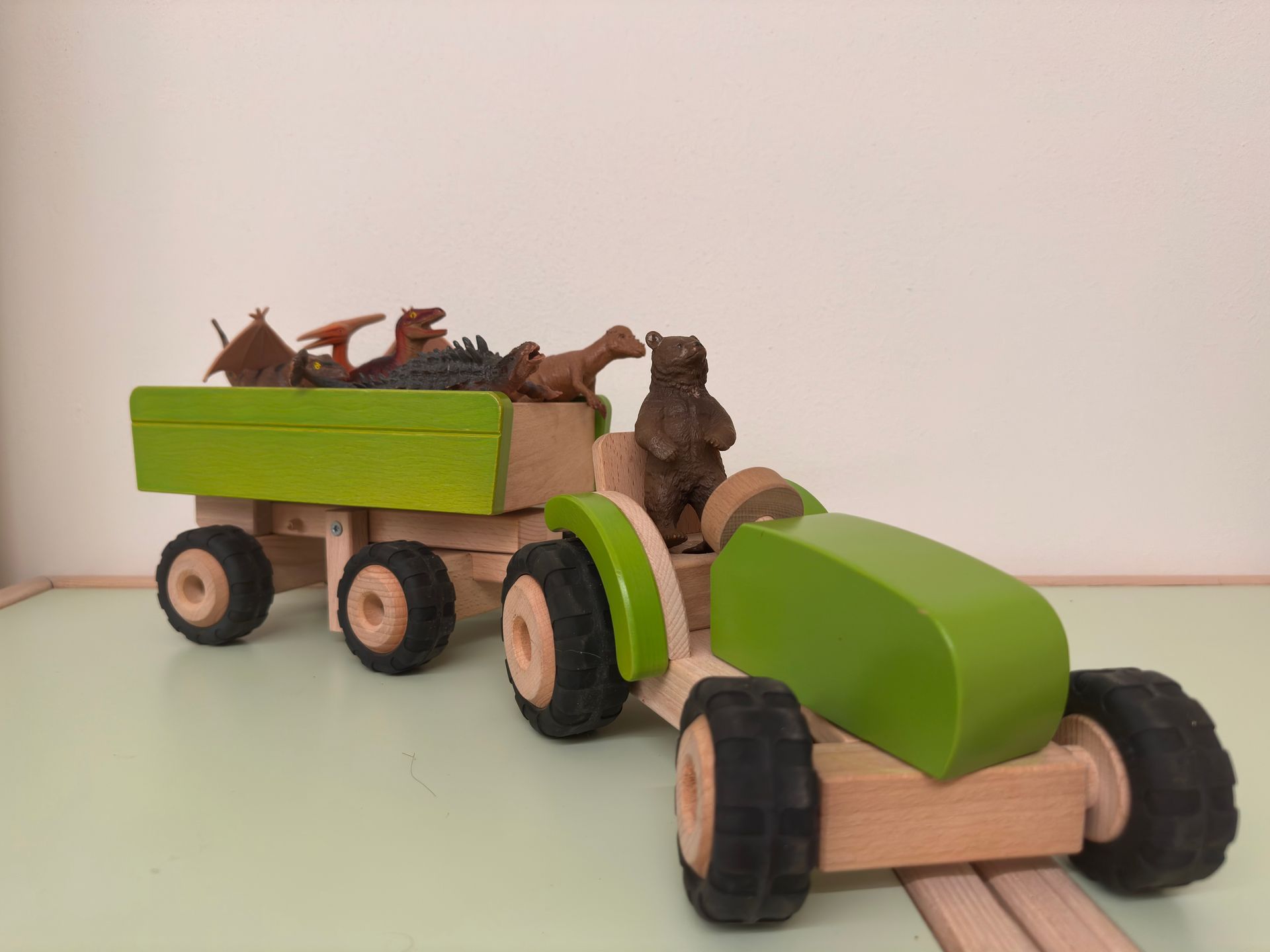 Trattore giocattolo di legno che traina un carro verde pieno di animali giocattolo.