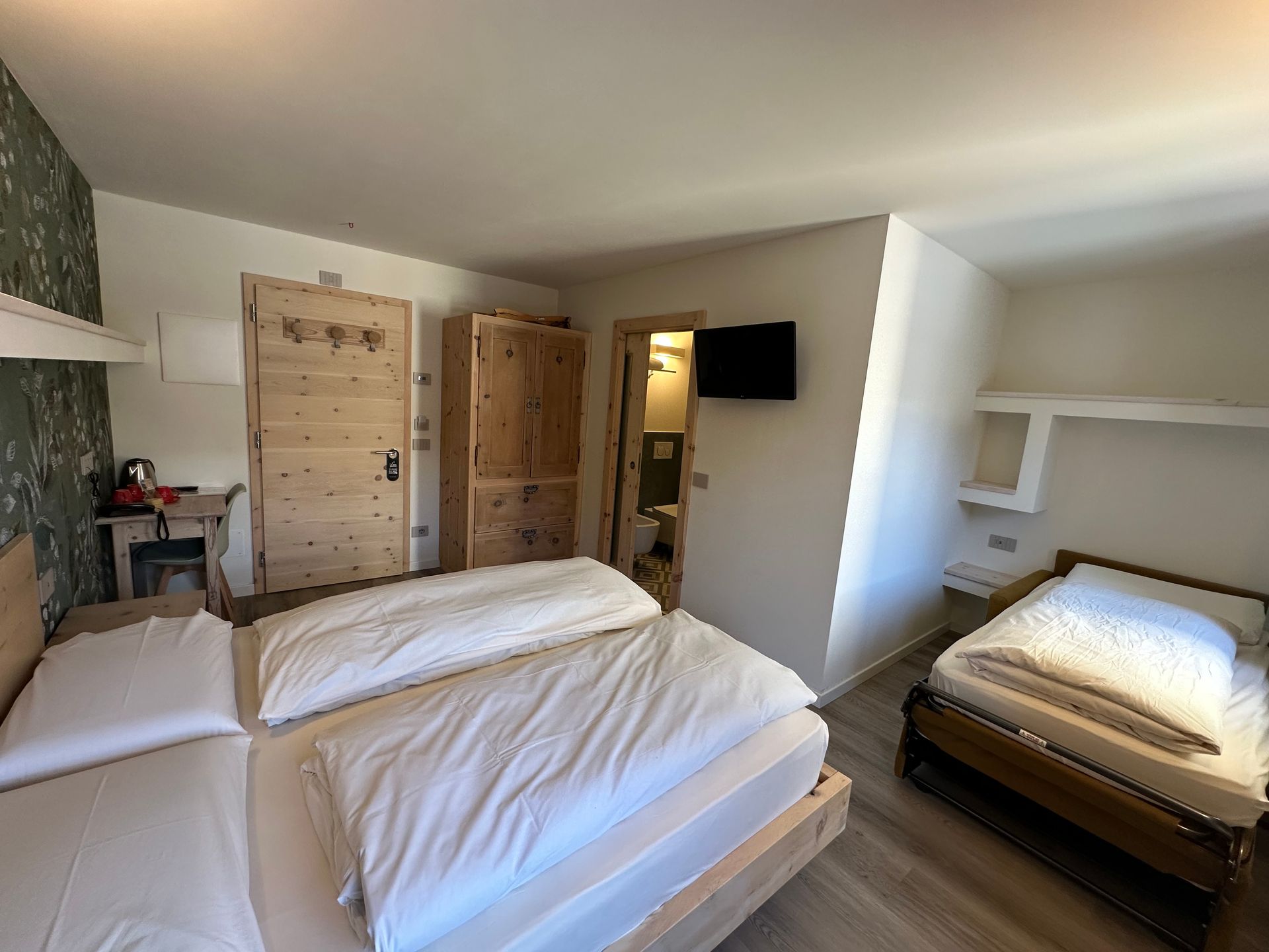 Camera da letto con tre letti, mobili in legno e una piccola TV. È visibile la porta del bagno.