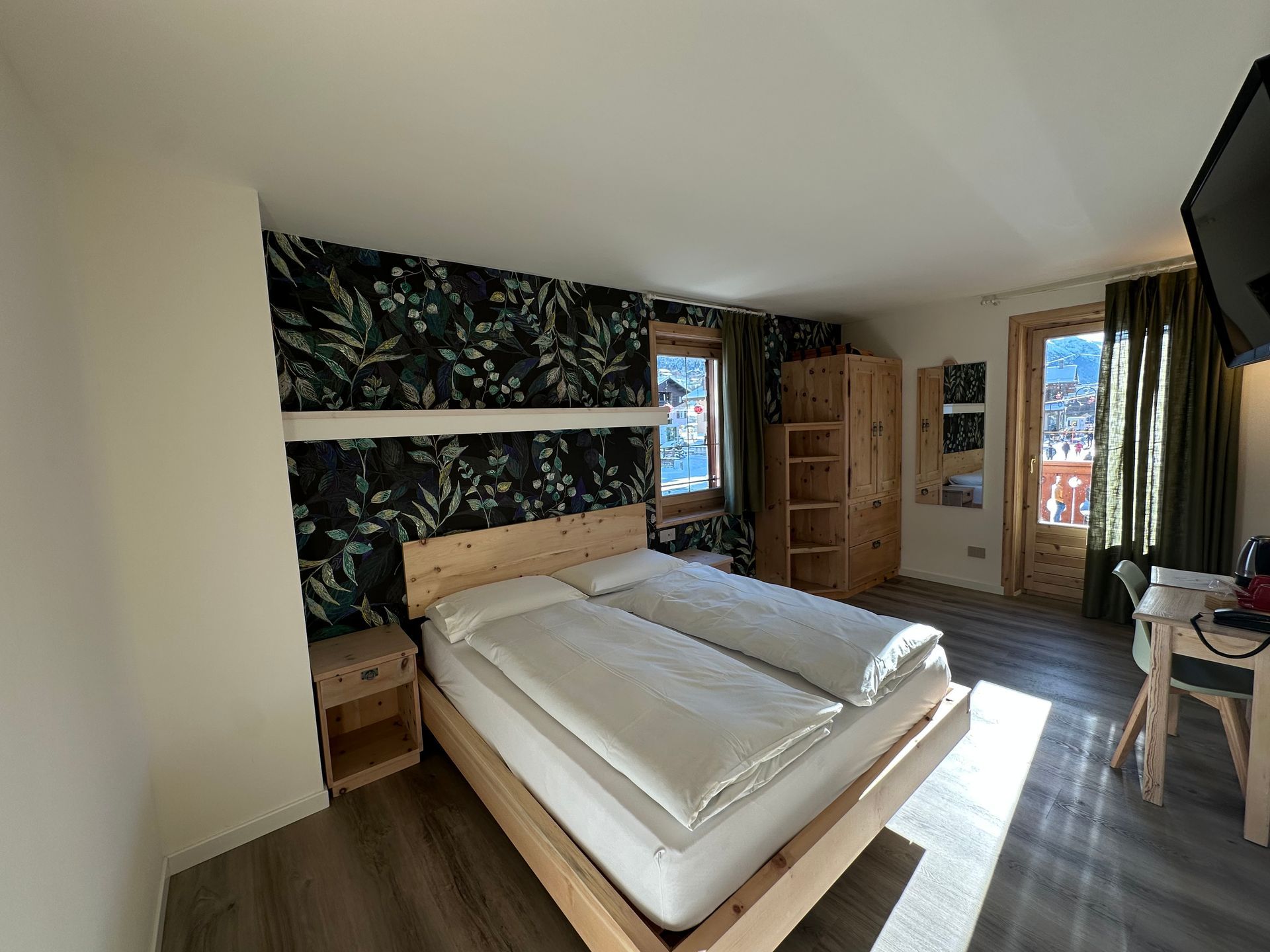 Camera da letto con letto matrimoniale, carta da parati floreale, mobili in legno e finestra con vista su un paesaggio innevato.