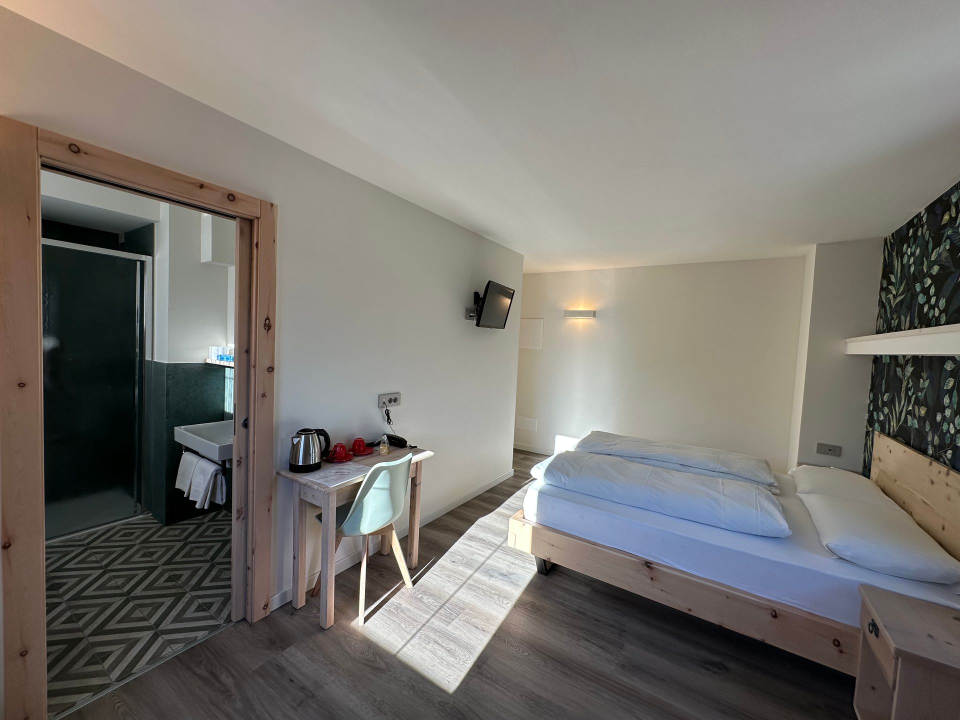 Camera d'albergo con letto, scrivania e bagno visibili sulla porta.