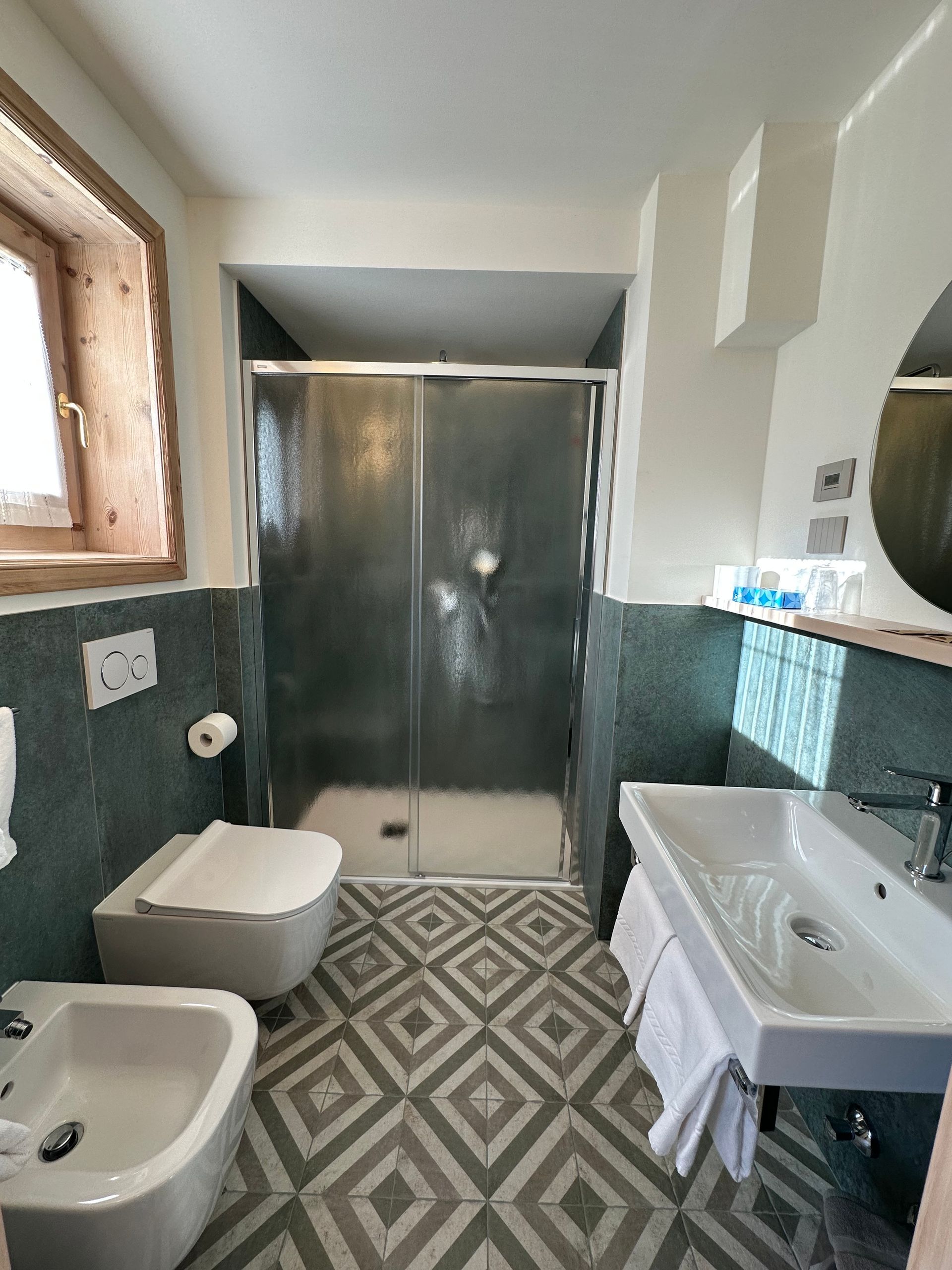 Bagno con doccia, WC e lavandino. Pareti piastrellate color verde acqua e pavimento a rombi grigi e bianchi.