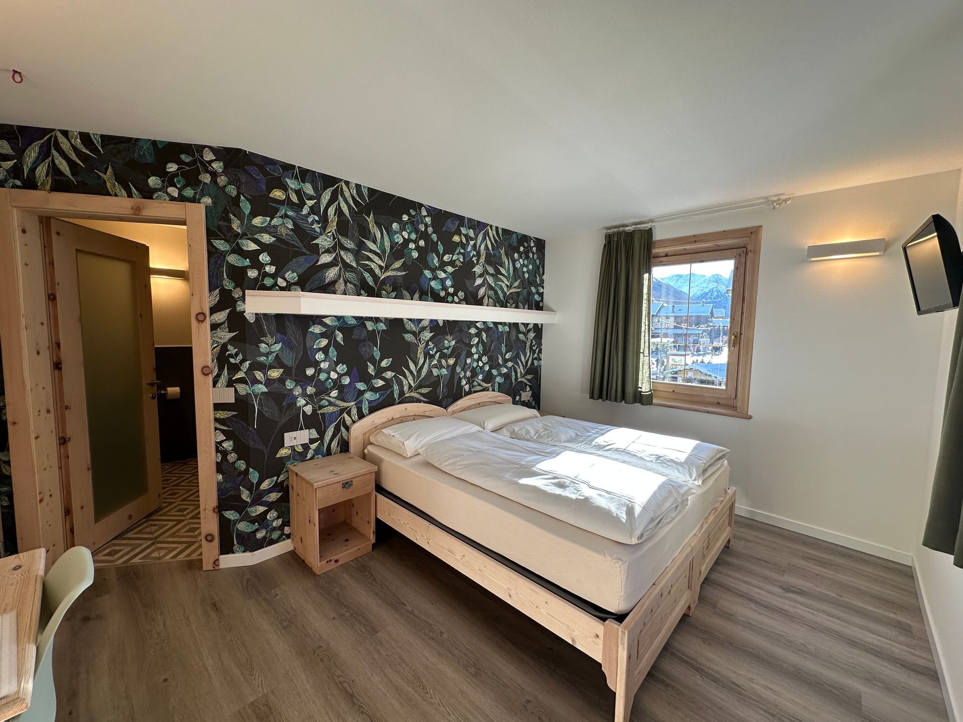 Camera da letto con carta da parati floreale, un letto e una porta che conduce al bagno.