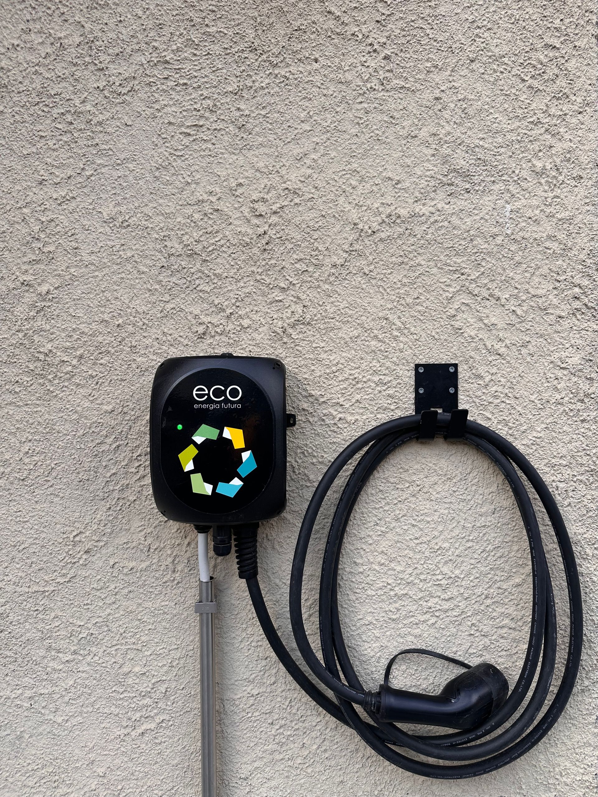 Caricabatterie per veicoli elettrici nero con cavo e supporto collegati su una parete strutturata.