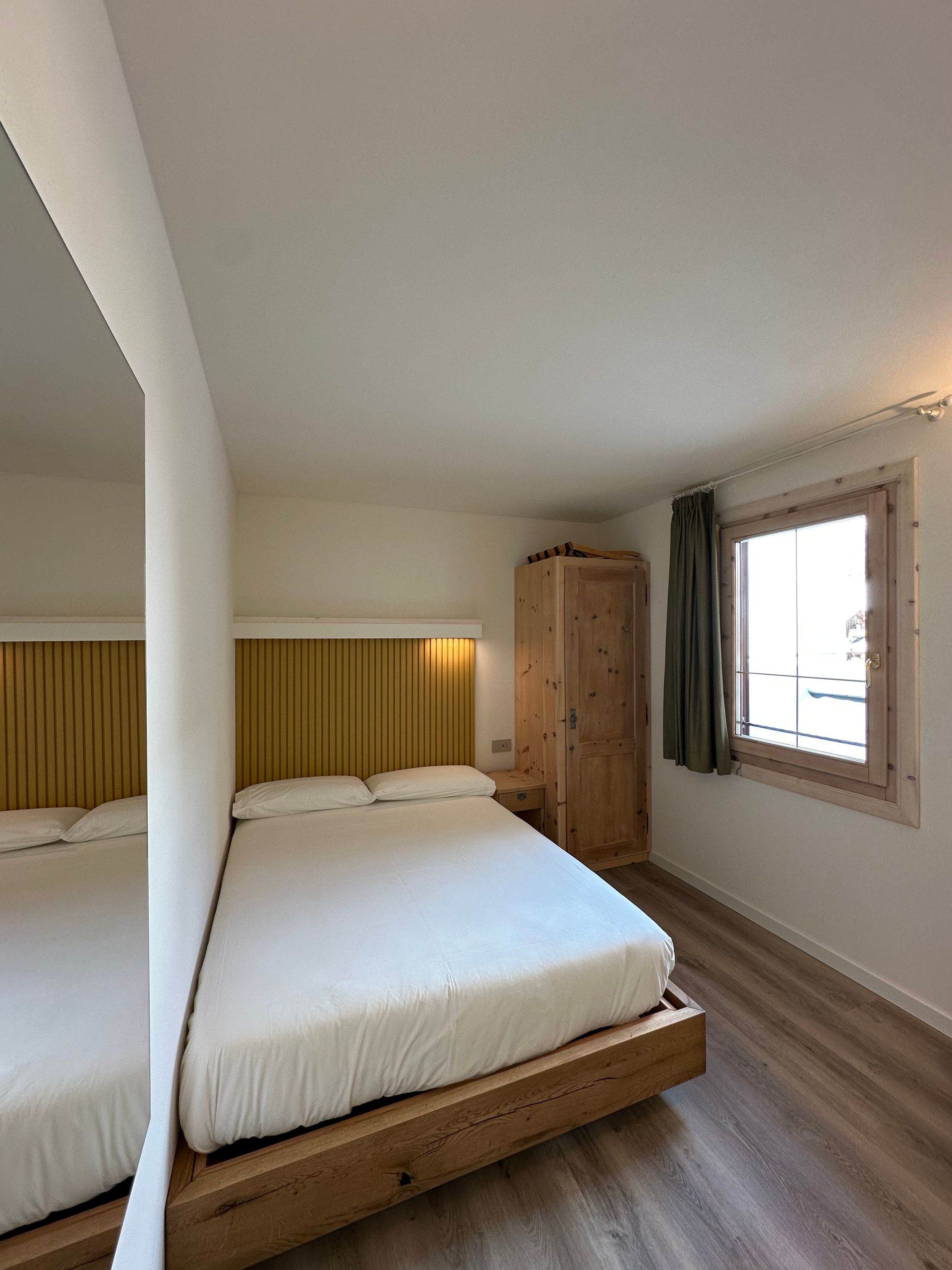 Camera da letto con letto matrimoniale, mobili in legno e finestra con tenda verde.