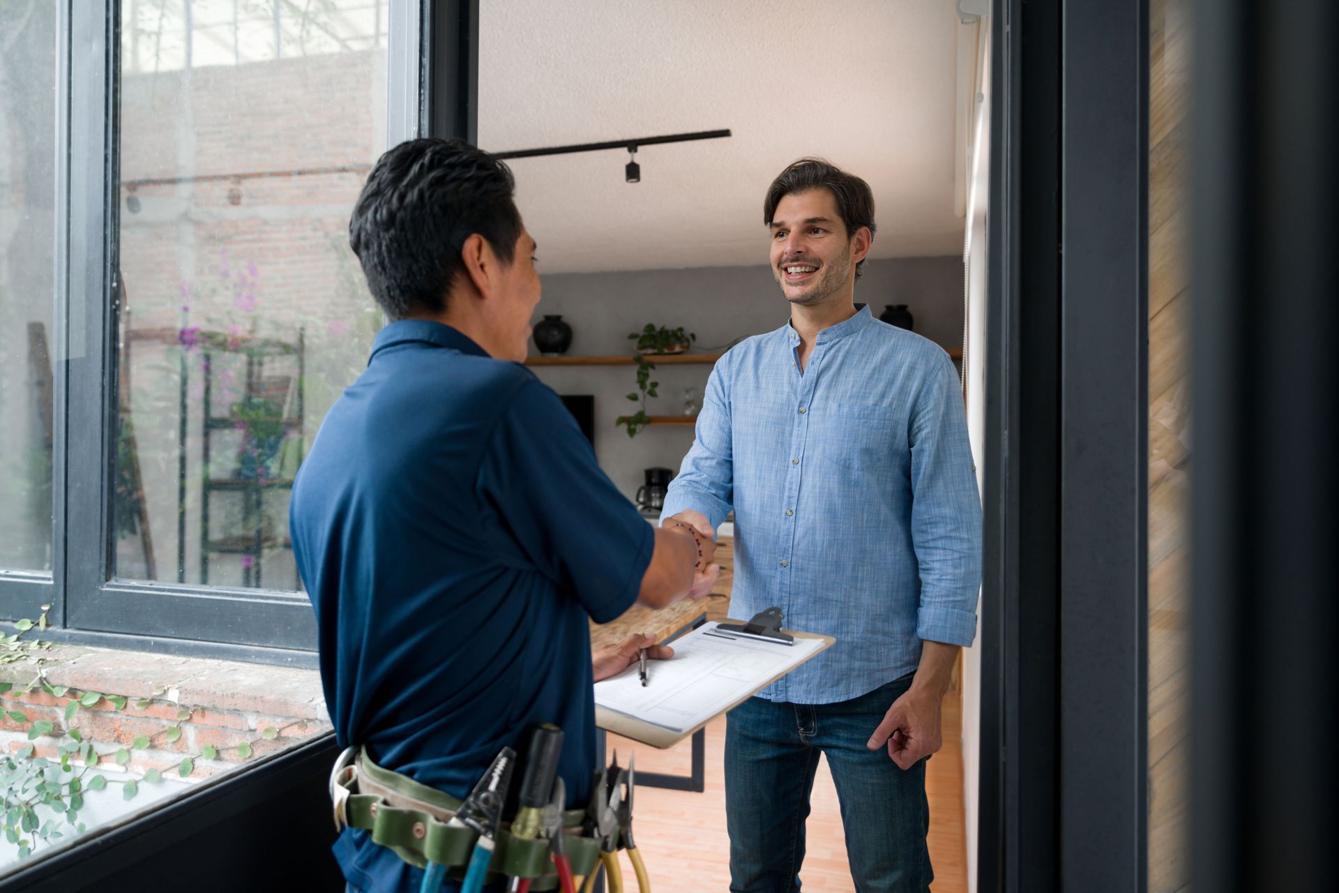 A plumber, about to perform residential plumbing service, is greeting a client with a handshake.