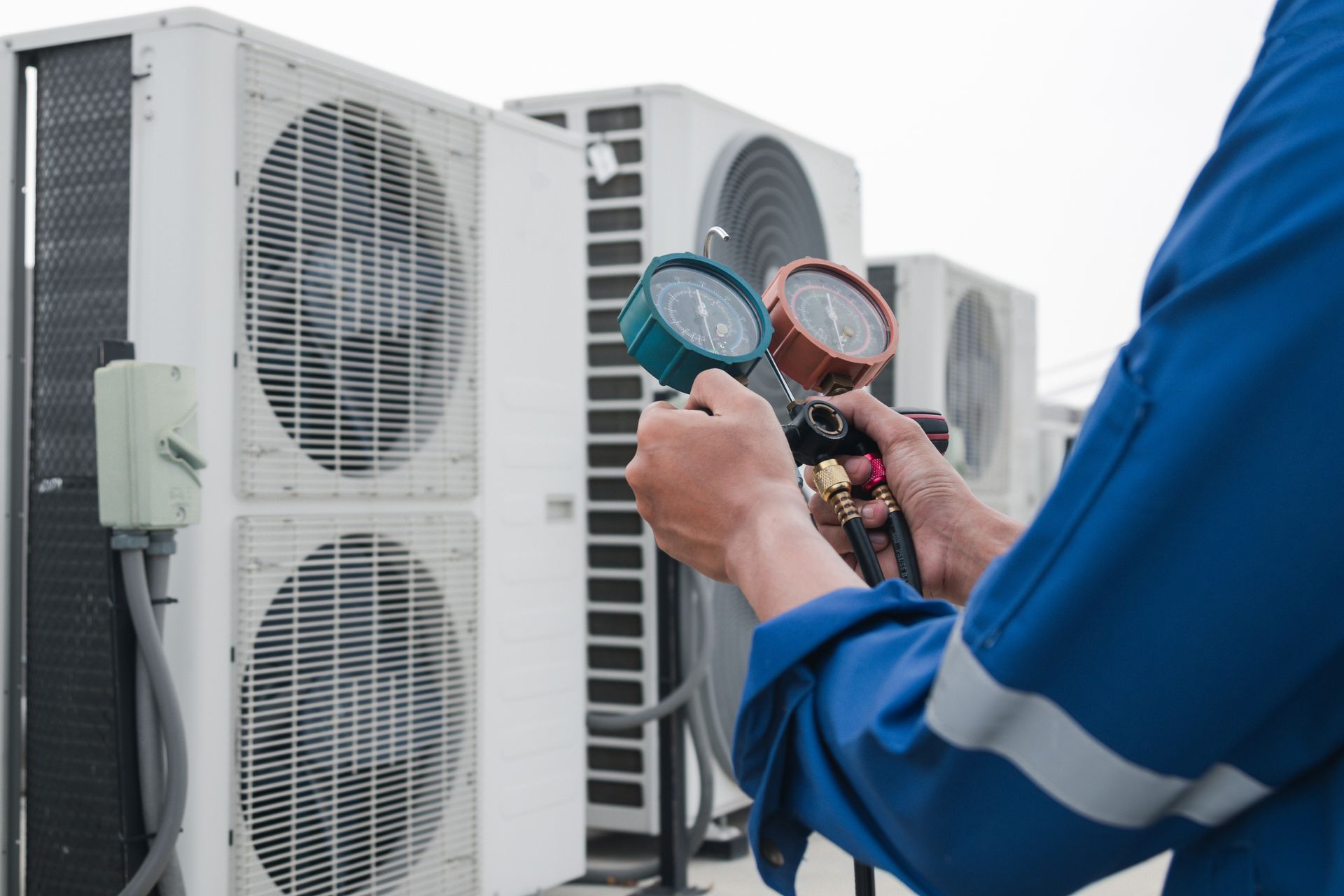 Technician using pressure gauges to check outdoor HVAC units during maintenance.