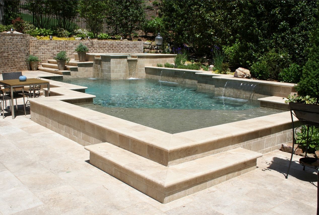 Stone pool with cascading waterfalls, steps, and patio furniture.