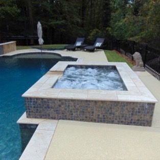 Poolside hot tub with bubbling water, surrounded by tile and lounge chairs.