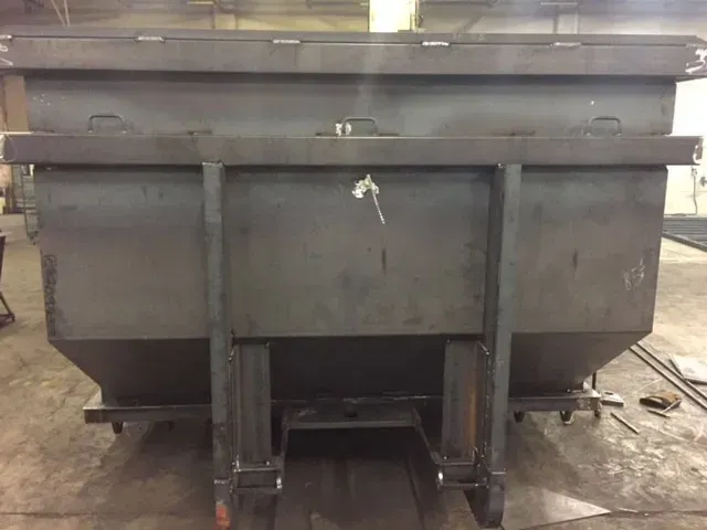 A large metal dumpster is sitting on the ground in a warehouse.