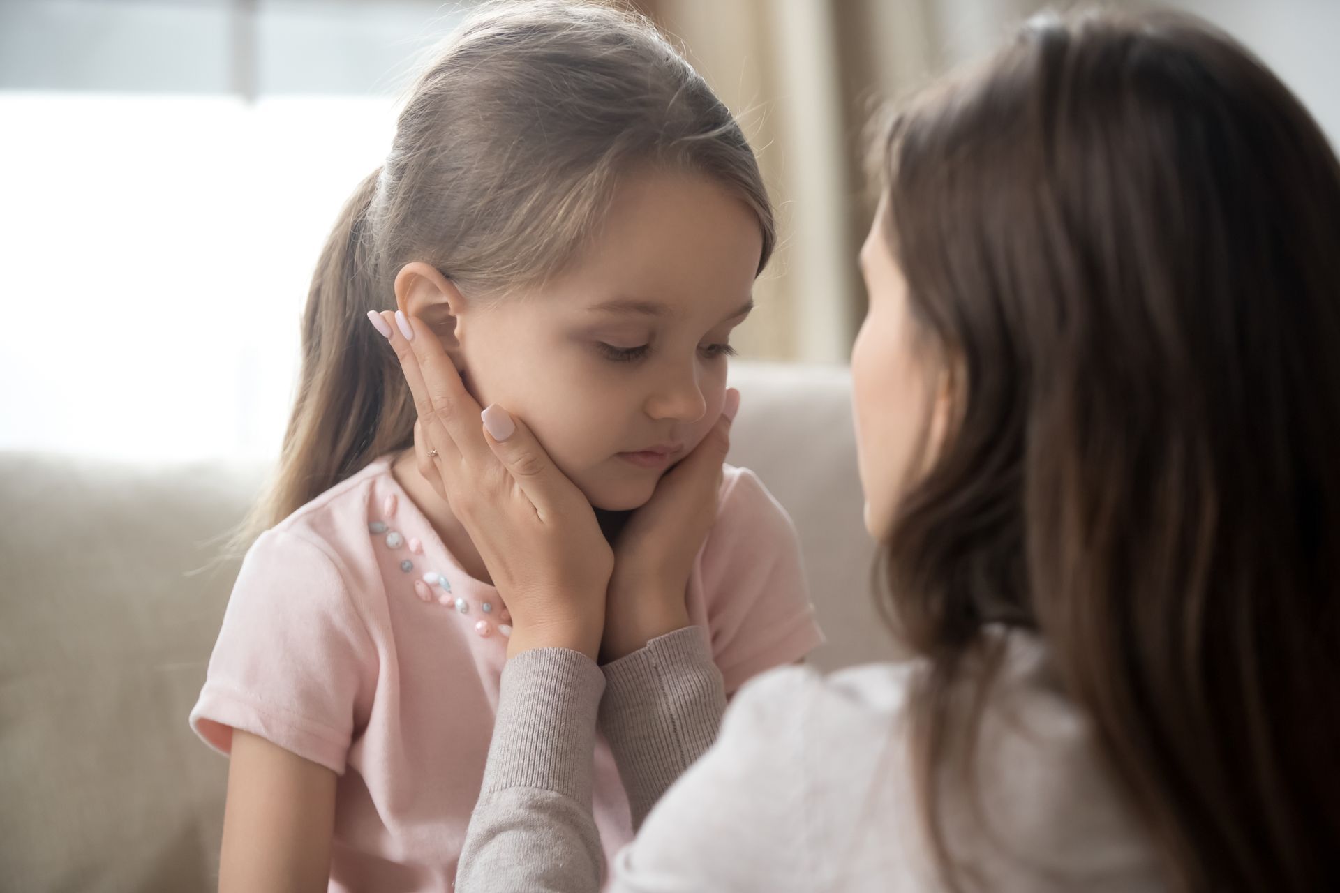 Woman comforting a young girl, gently cupping her face indoors.